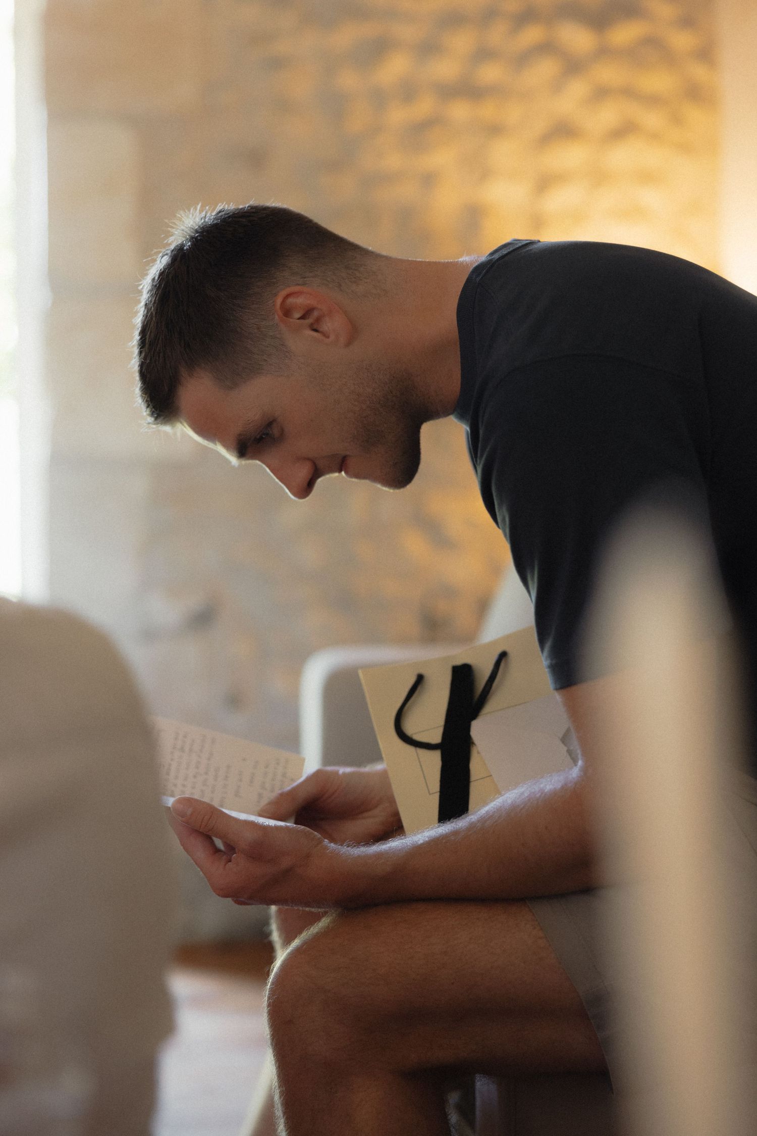 Person in black shirt reading document in warm indoor lighting.