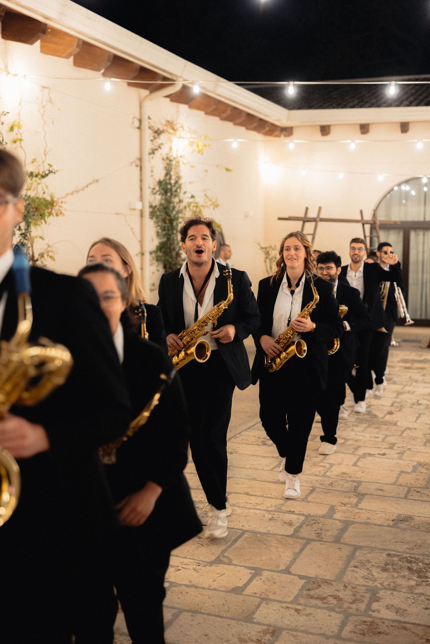 Wedding party band members in black suits perform music at an elegant indoor reception venue.