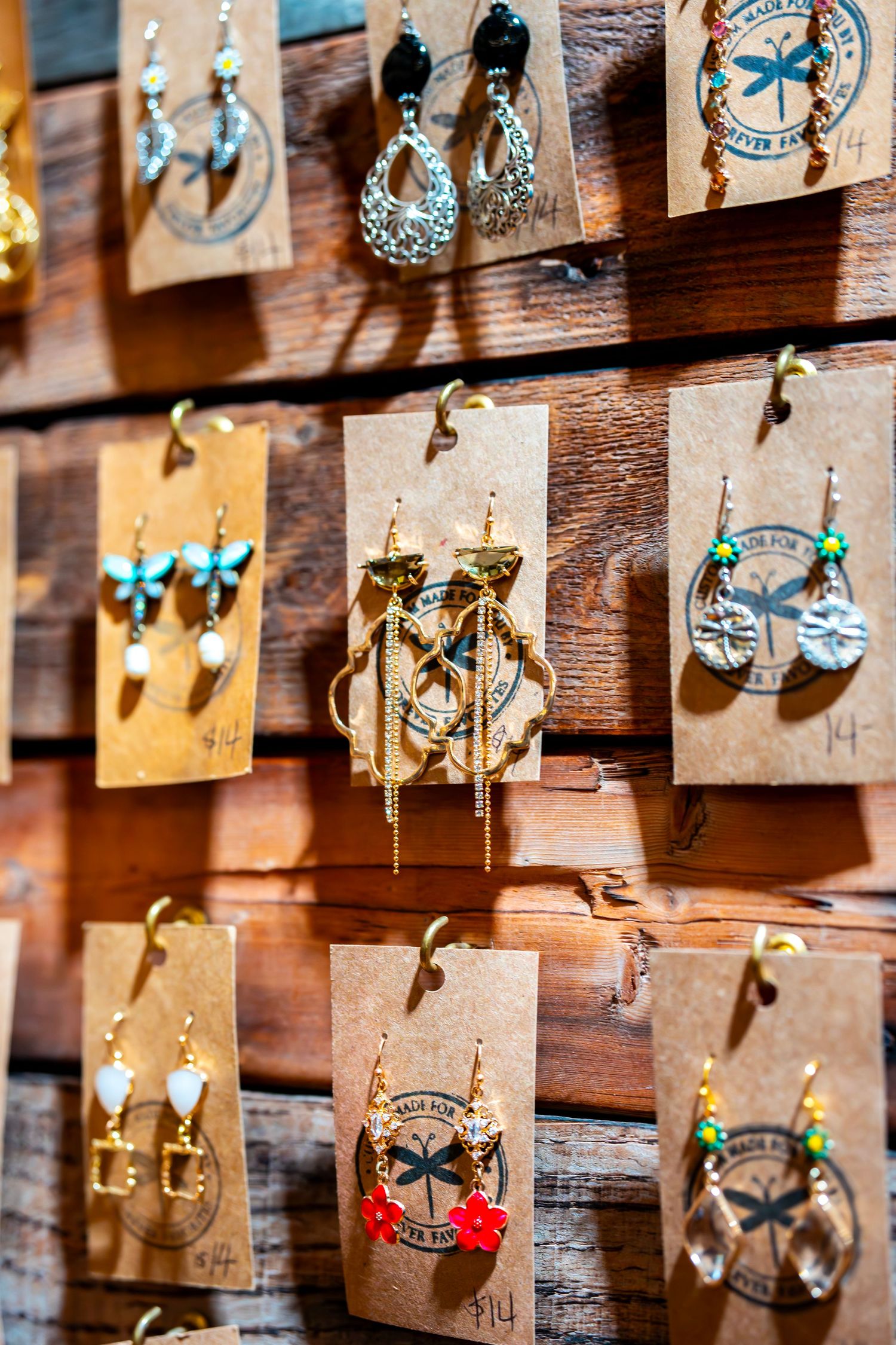 Handcrafted earrings with dragonfly designs displayed on kraft paper cards against wooden background.