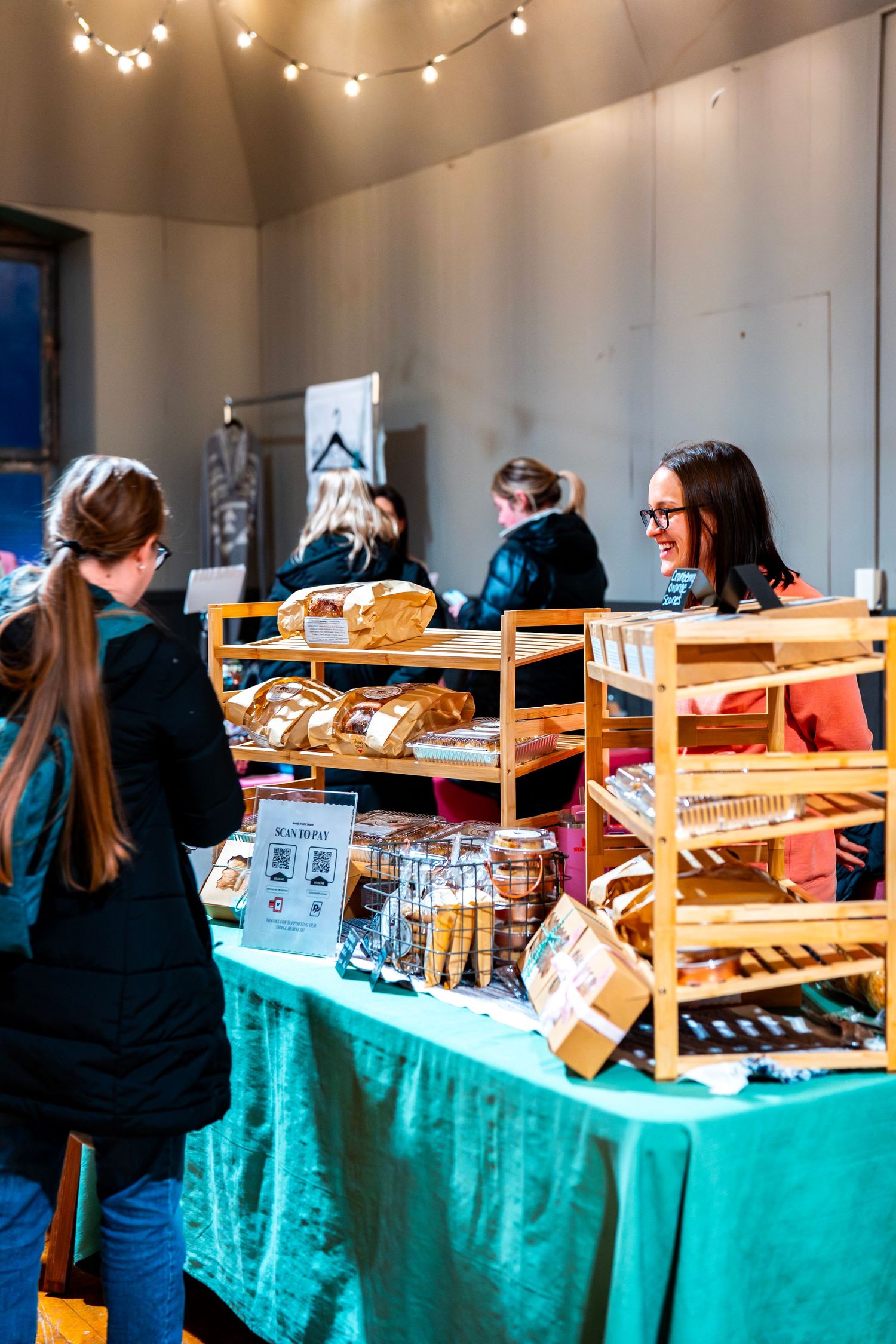 Market vendors displaying goods on wooden shelves covered with turquoise tablecloths.