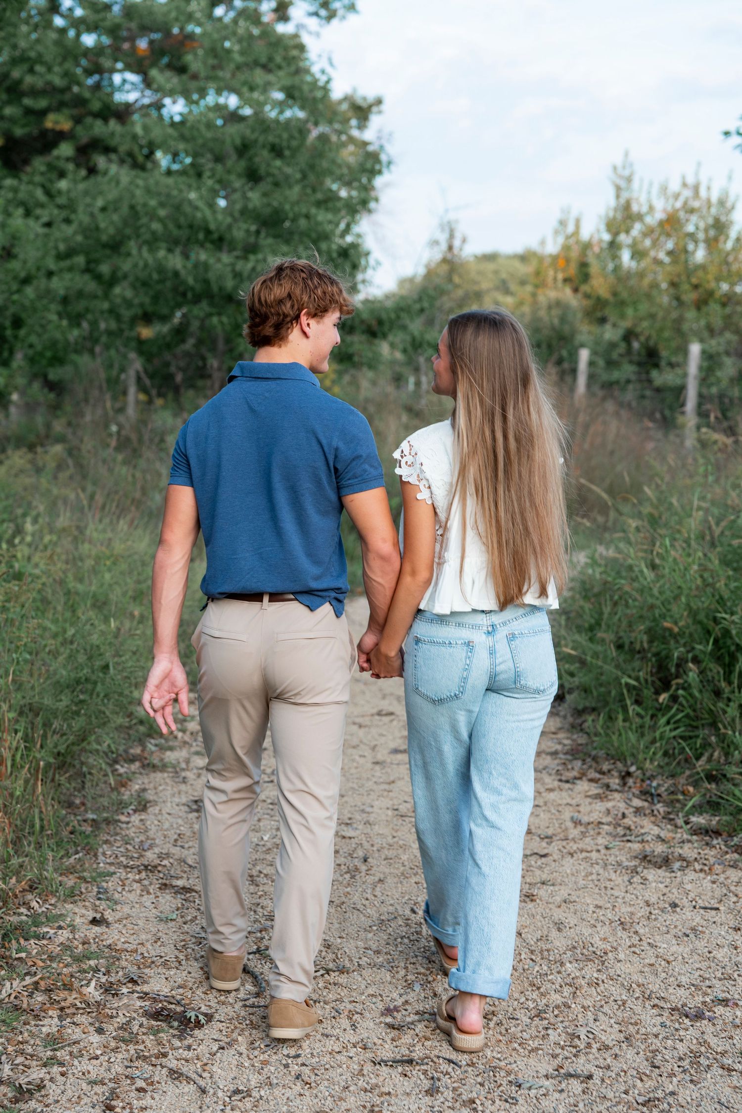 A couple walking together on a dirt path viewed from behind.