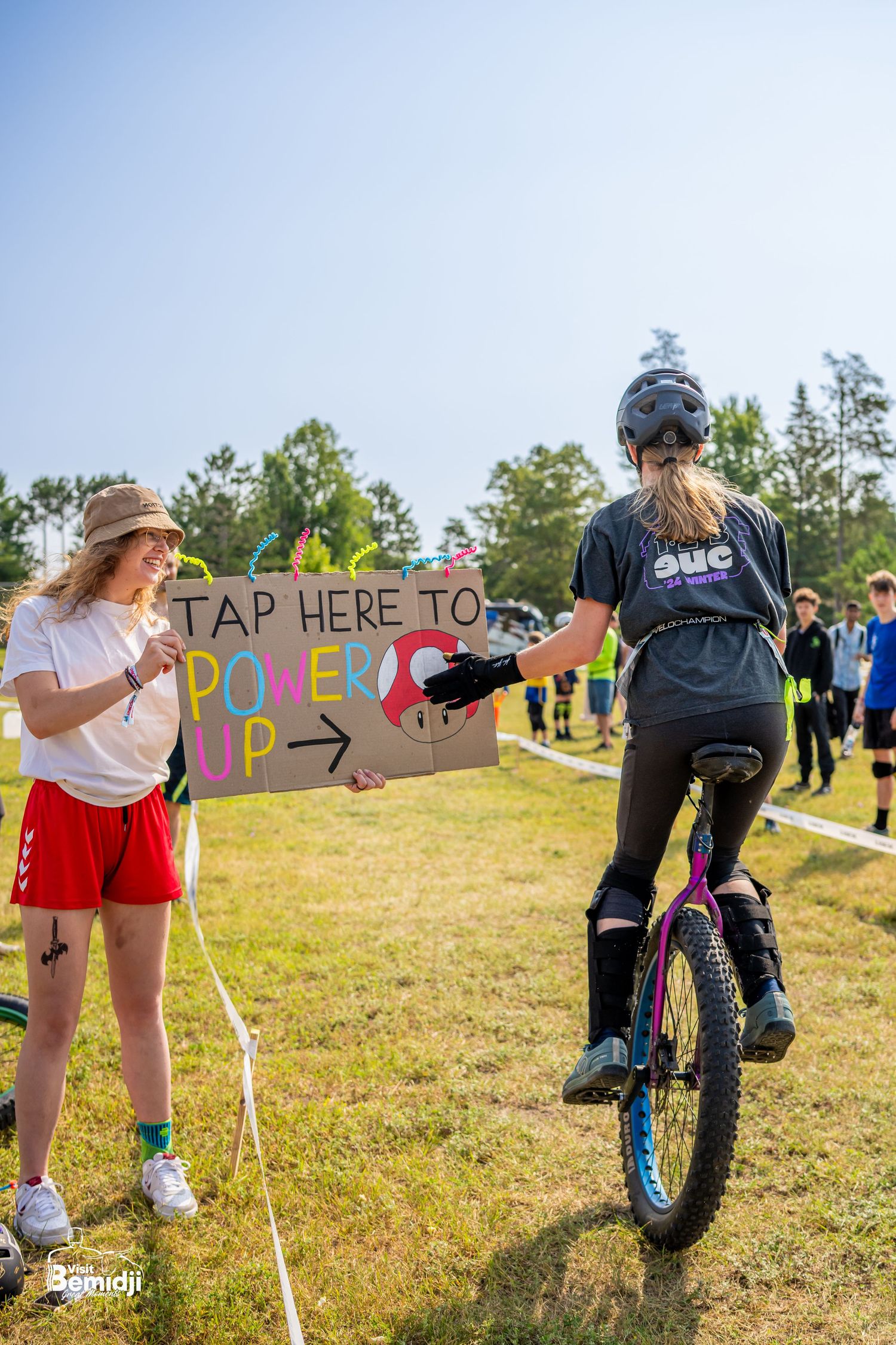 Cyclists gathering near colorful signs and course markers at an outdoor biking event cheering each other on.