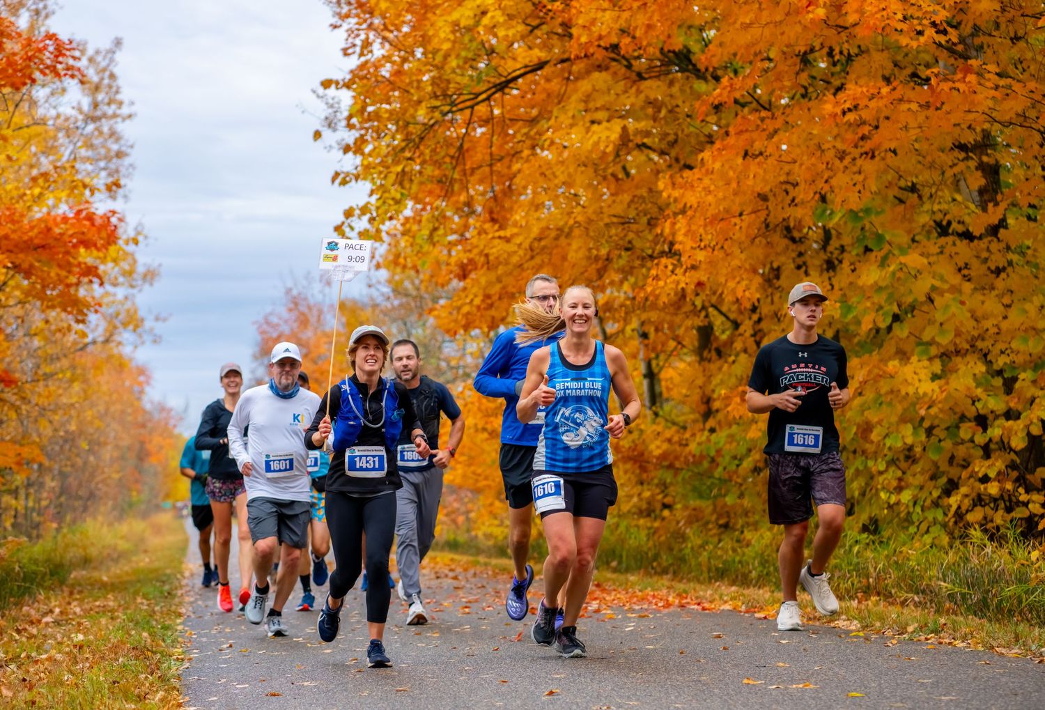 Group of runners participating in a fall marathon along a tree-lined path with vibrant autumn foliage.