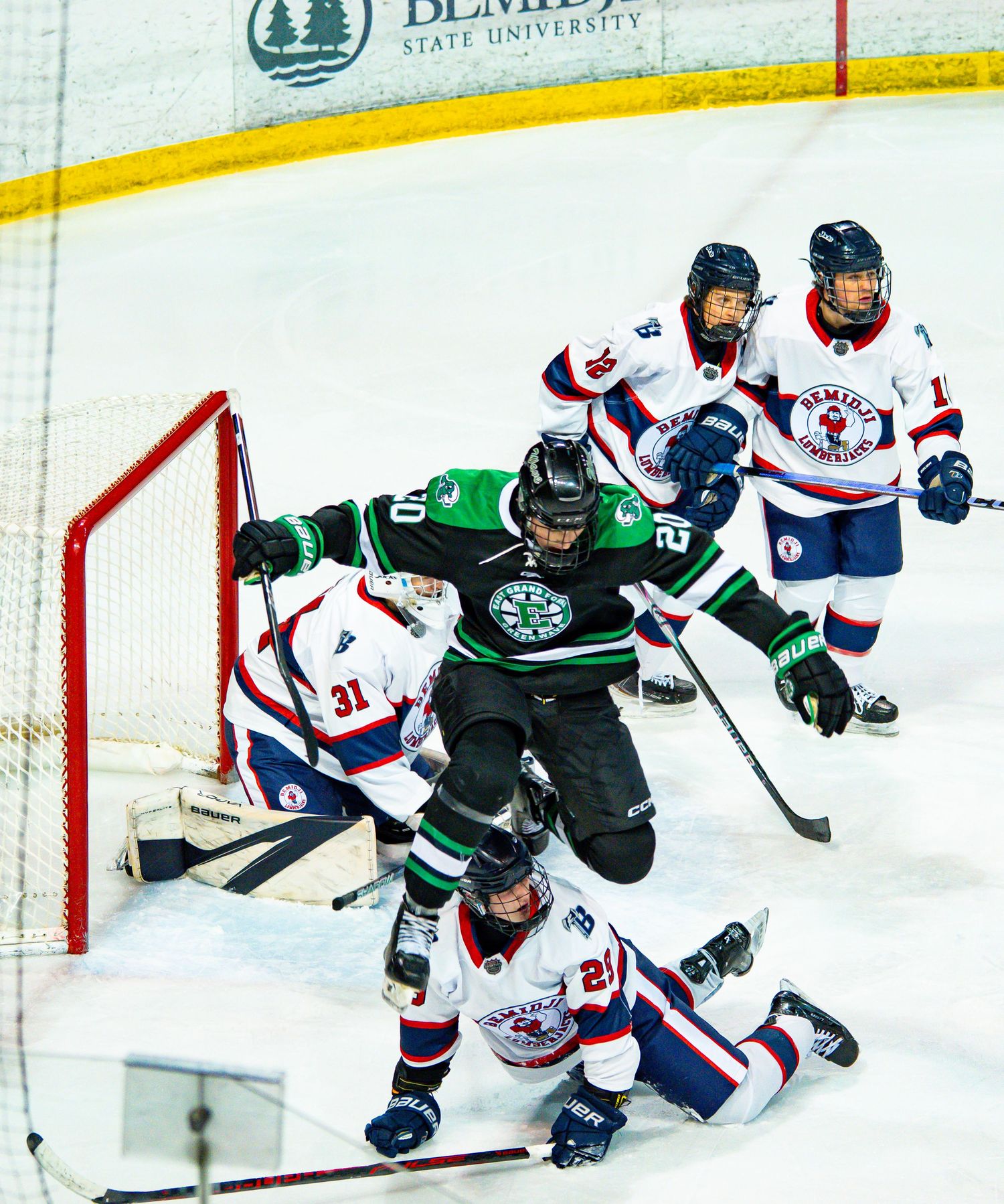 Hockey players from opposing teams facing off near the goal during an intense match.