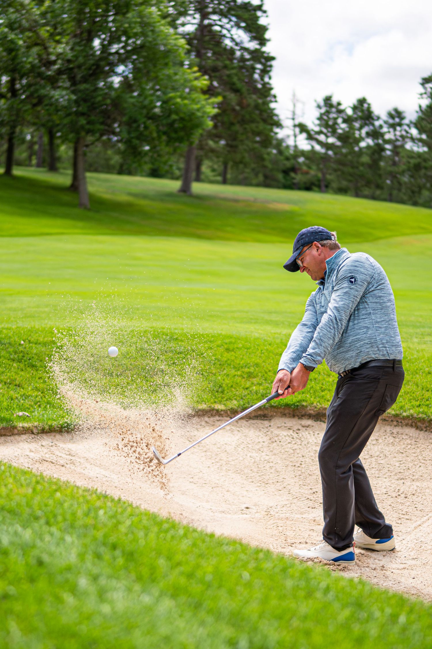 Golfer hitting ball out of sand bunker on lush green golf course.