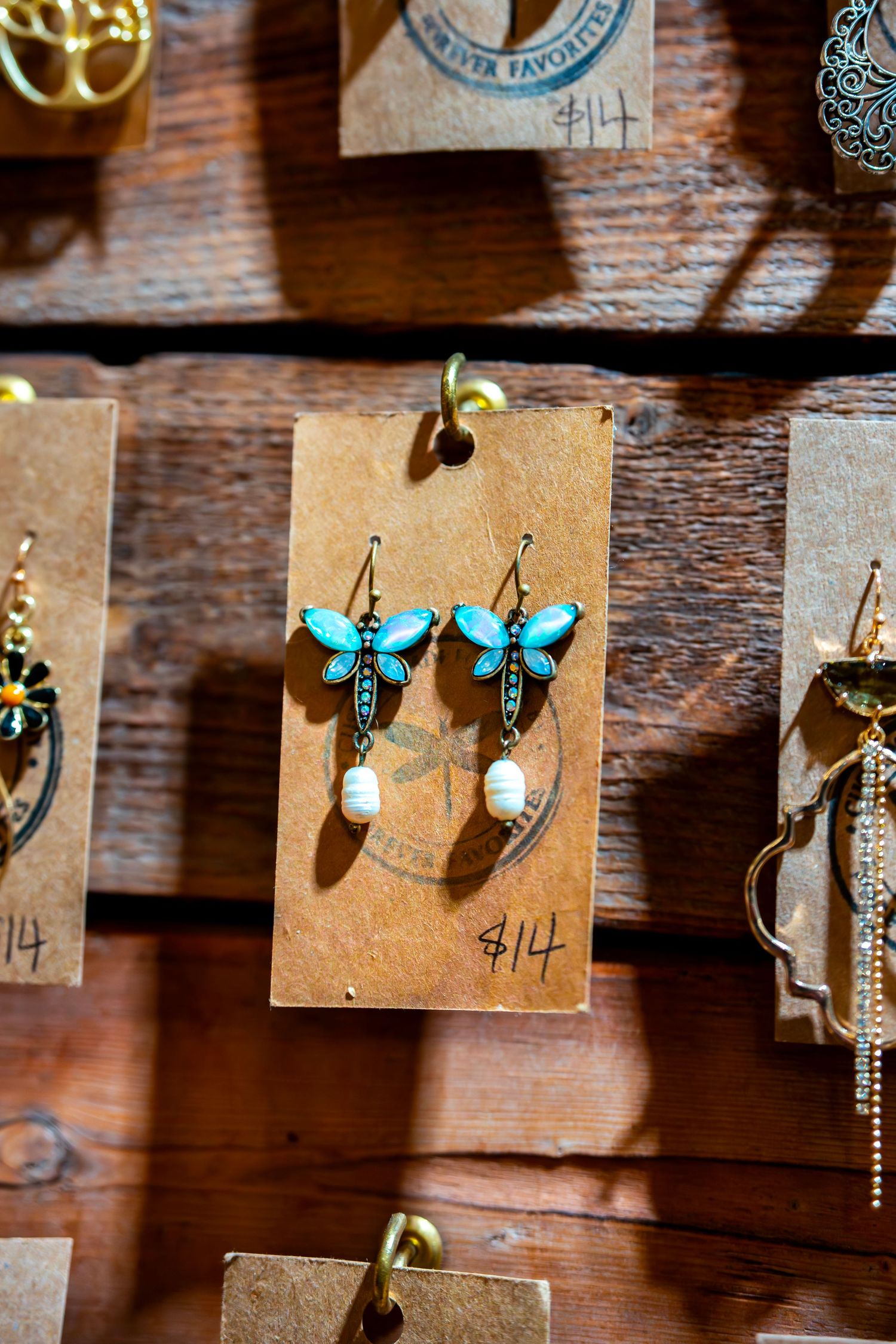 Artisan jewelry and earrings displayed on kraft paper cards against wooden background.