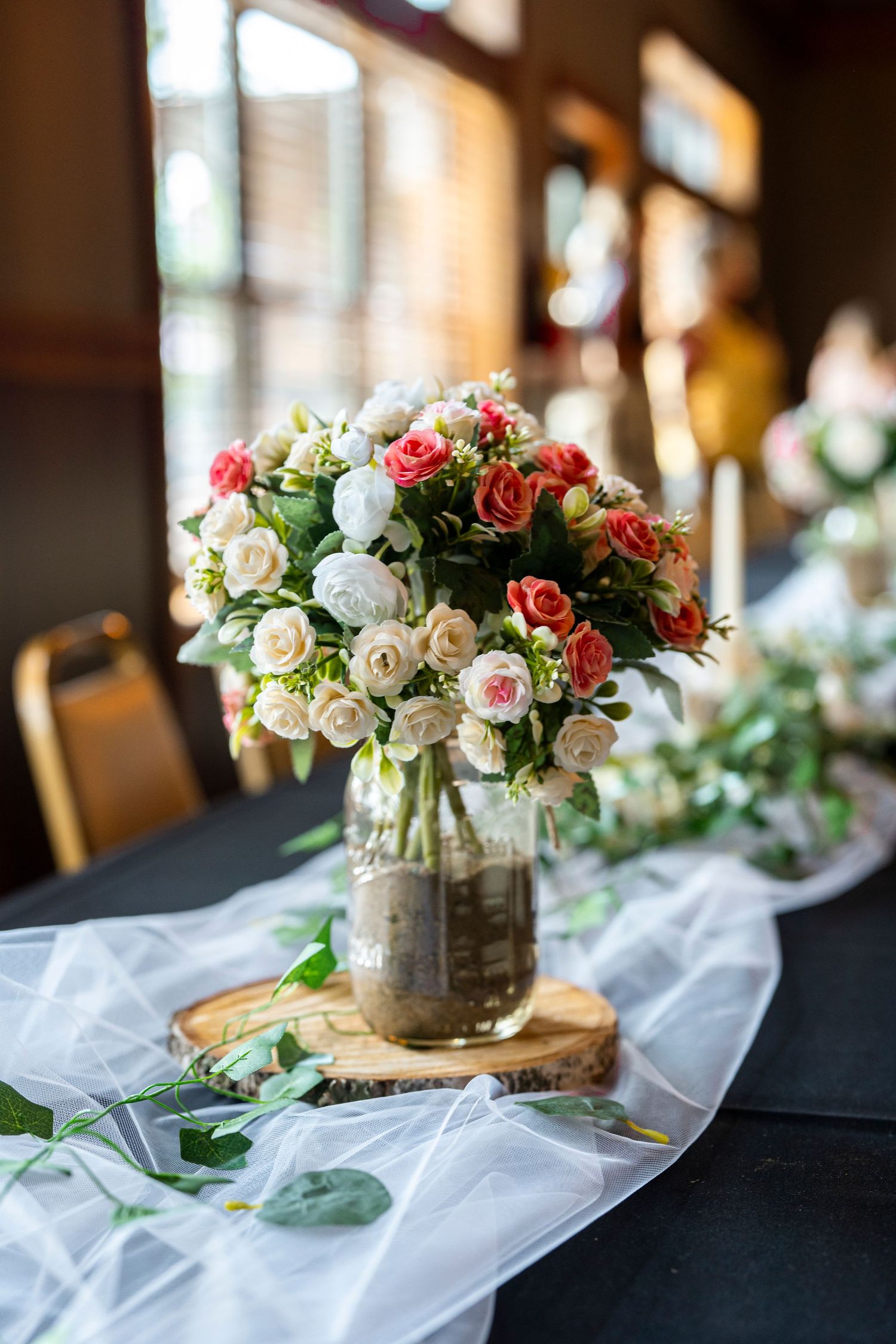 Rustic centerpieces with pink and white roses on wooden slices with tulle table decorations.