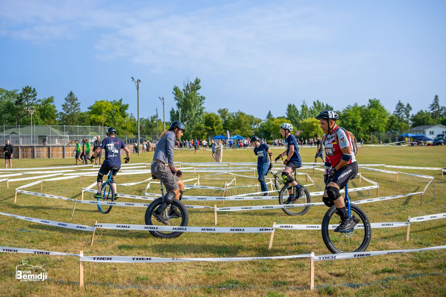 Cyclists navigating a winding course marked with white ropes on grass terrain.