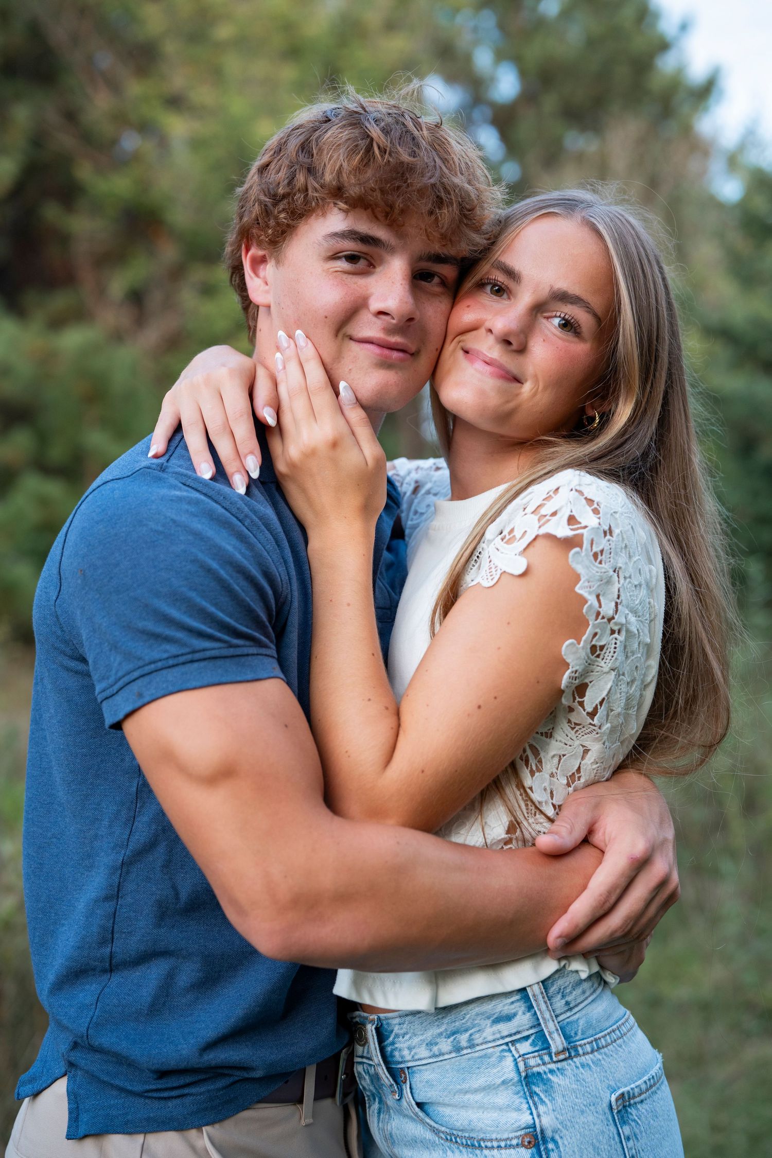 A playful couple embraces outdoors in casual attire against a natural background.