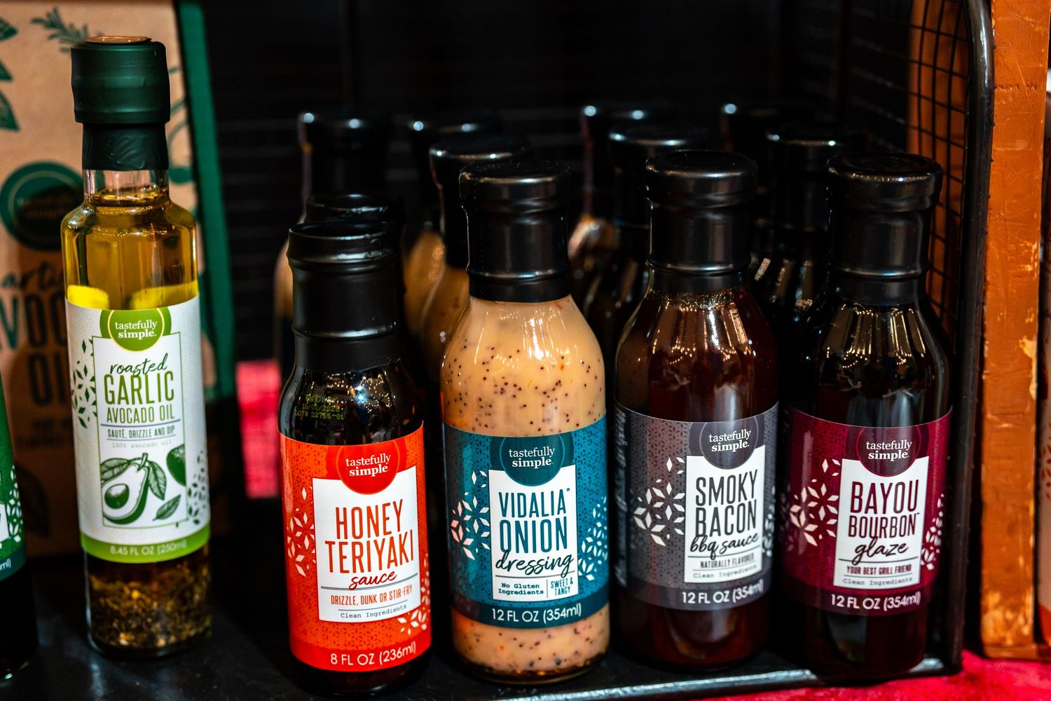 Row of bottled sauces and condiments displayed on wooden retail shelving.