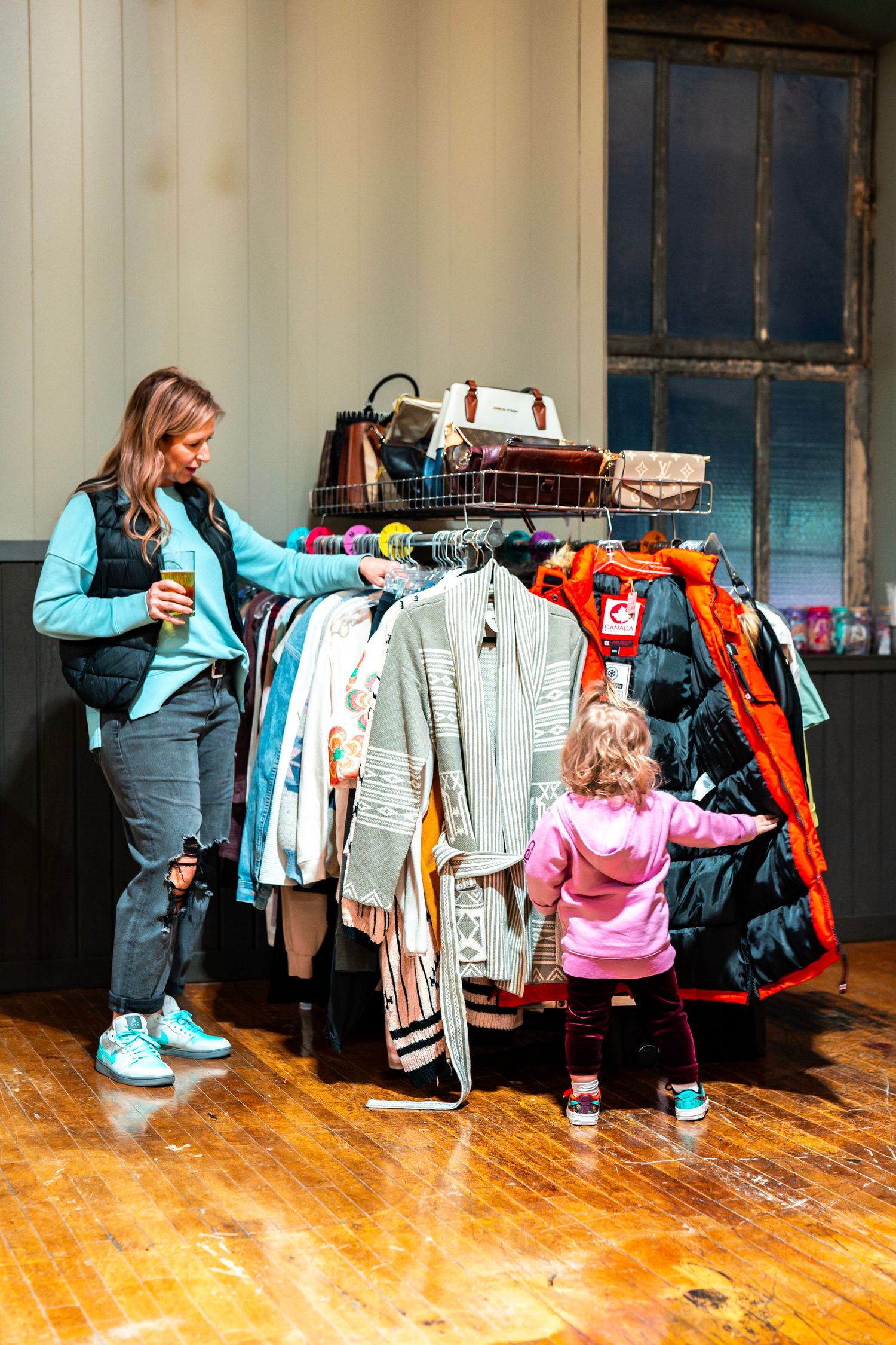 Clothing rack display with winter coats and accessories on a wooden floor at a retail event.