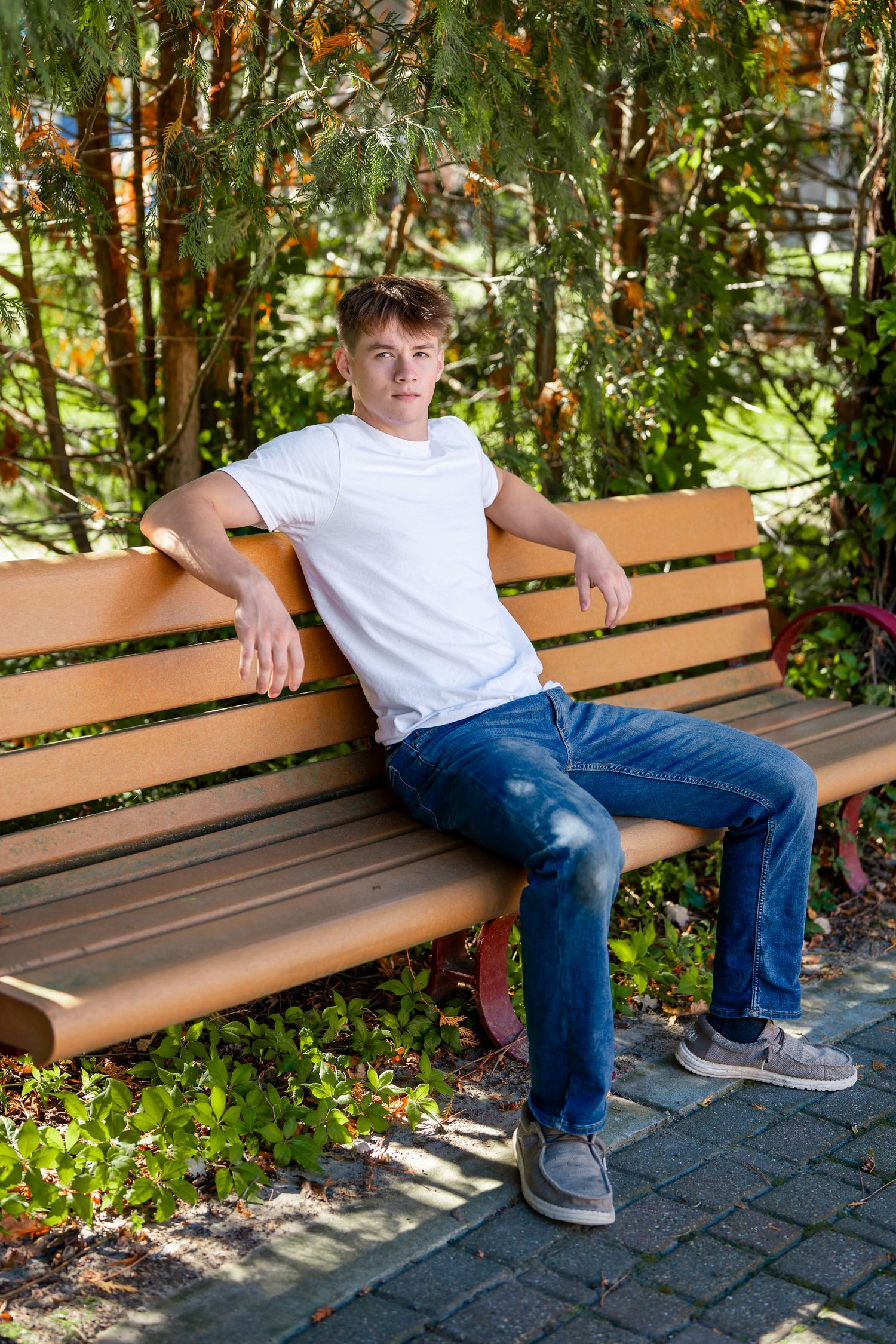 Young man in casual attire relaxing on wooden bench in garden setting.