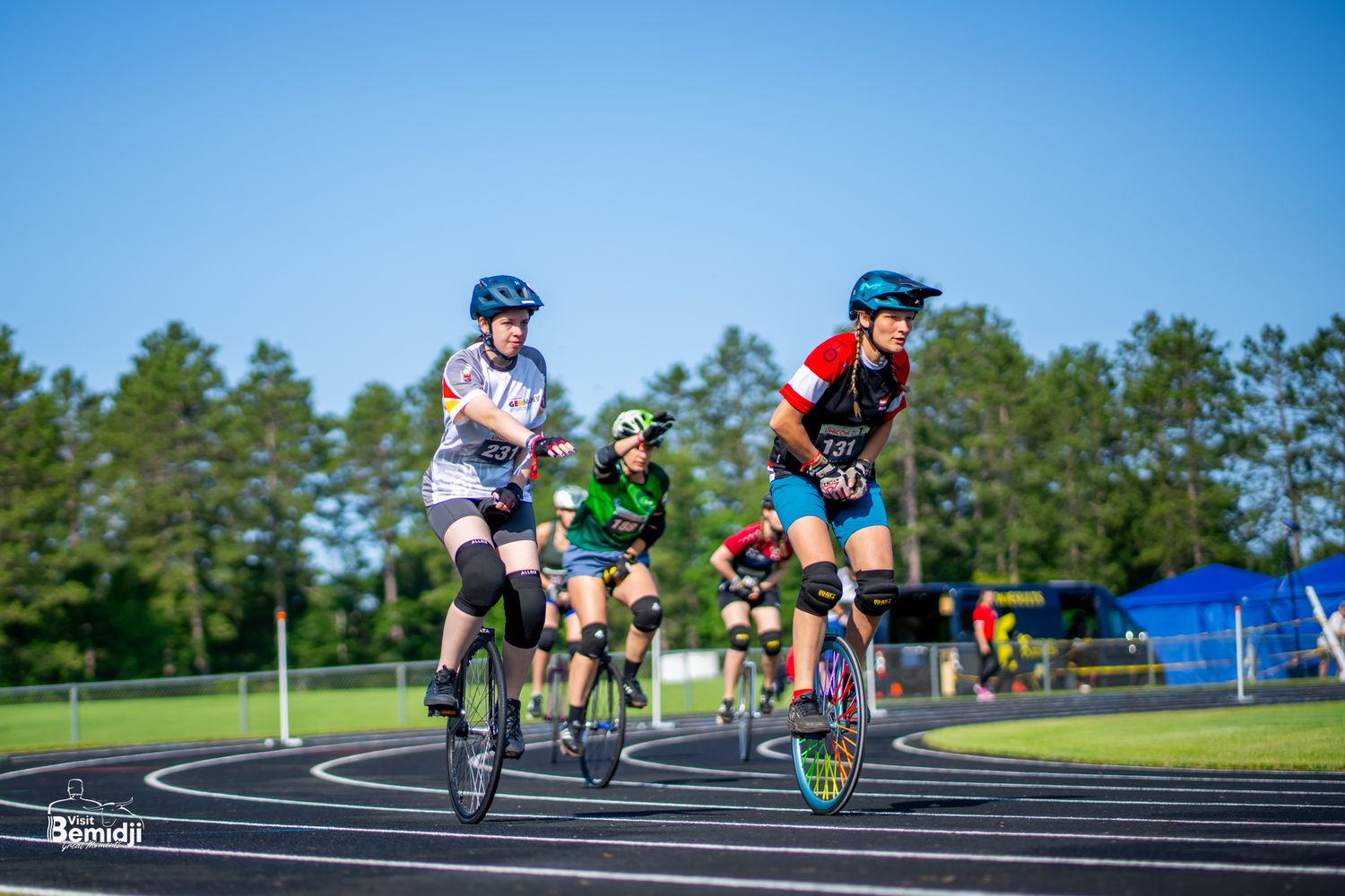 Unicyclists racing on outdoor track during daytime competition.