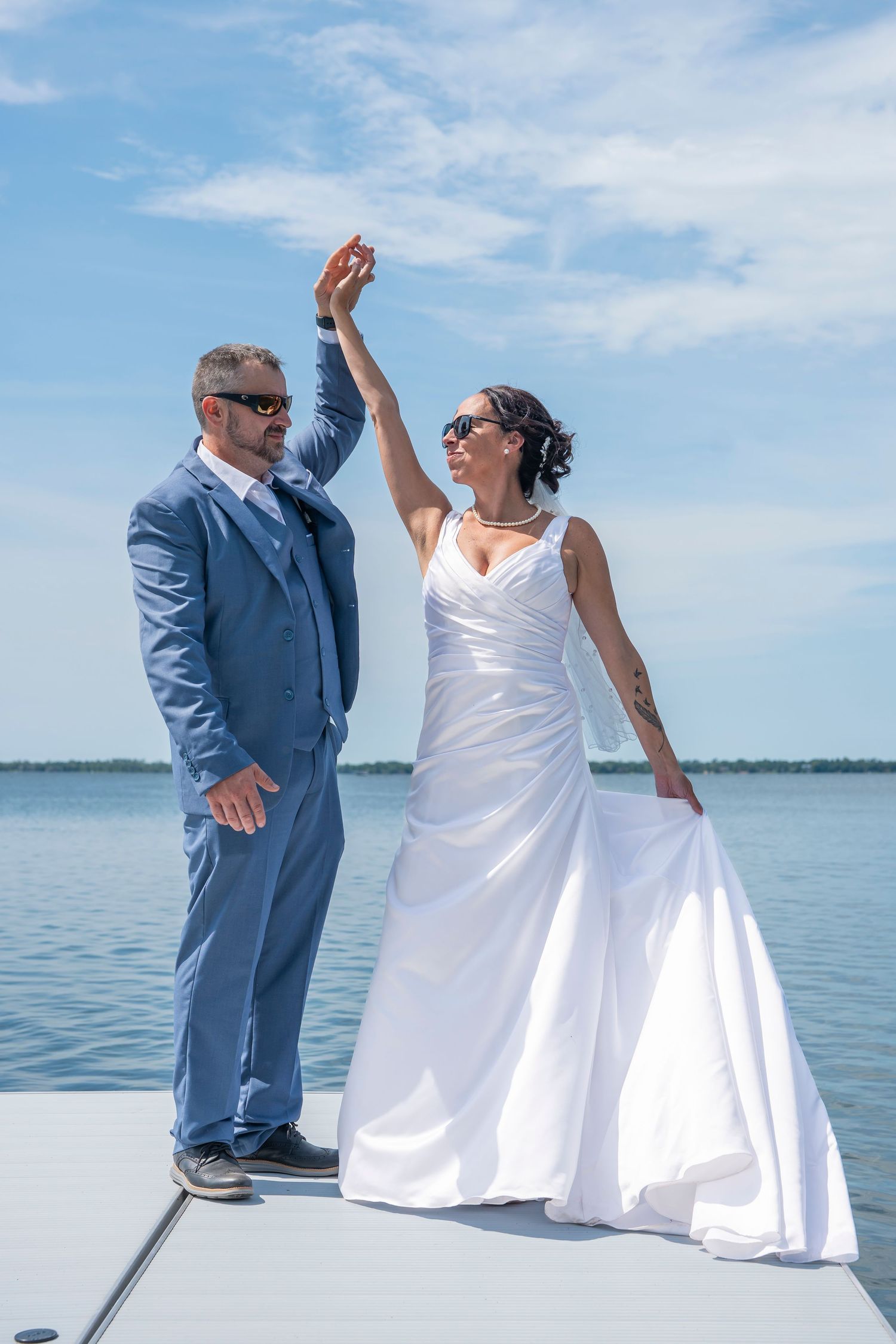 A playful wedding couple dances and poses on a white dock by the water on their special day.