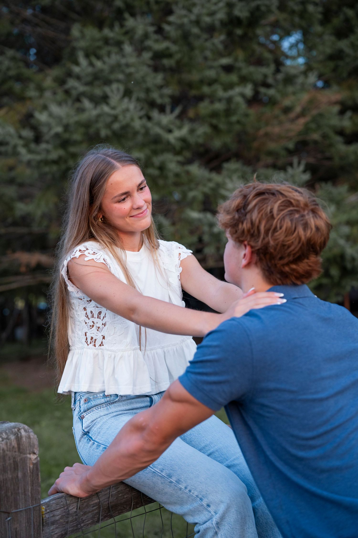 A couple in casual attire shares a playful moment together outdoors on a fence.
