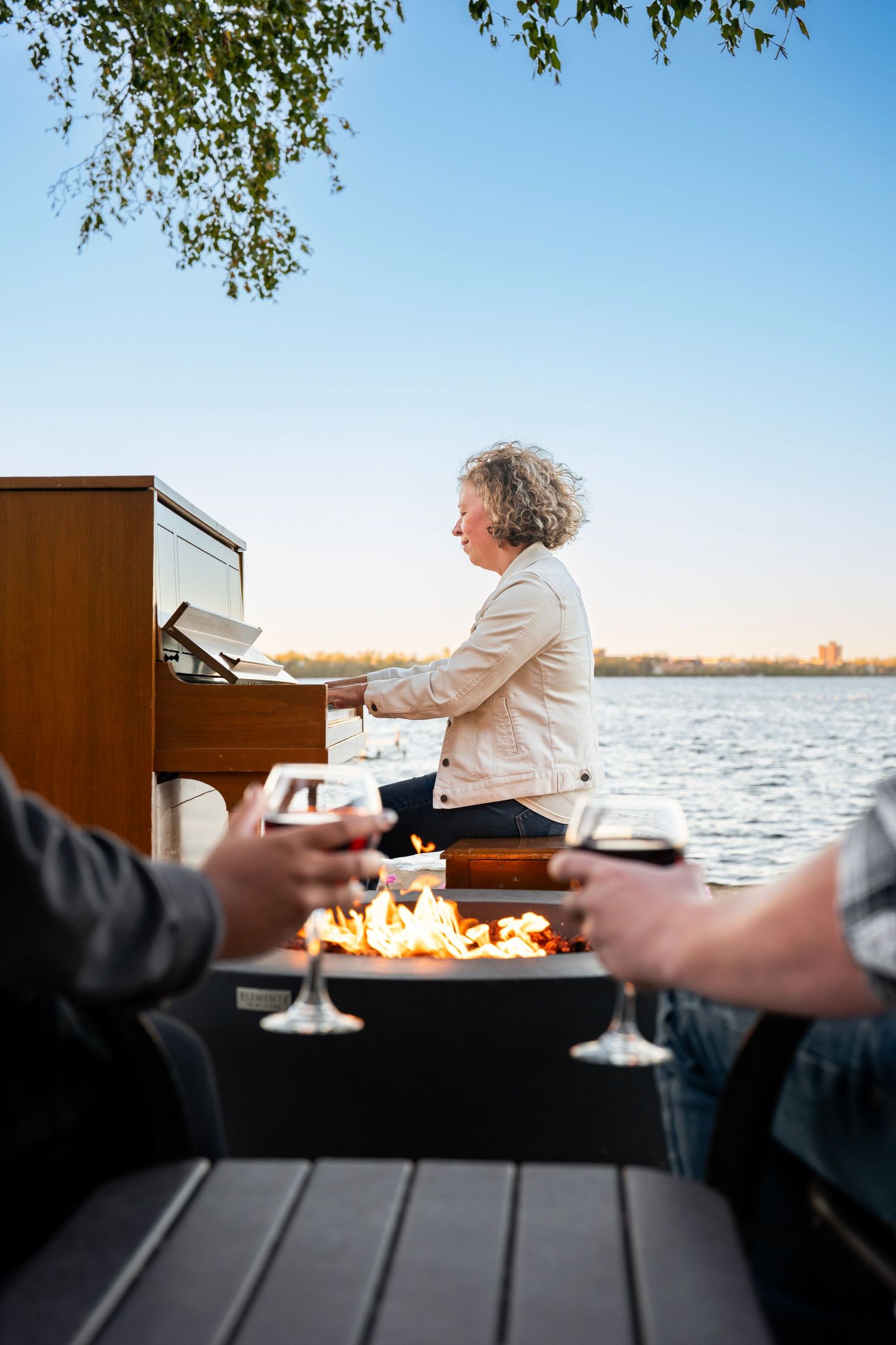 Piano performance by waterfront with wine glasses in foreground.