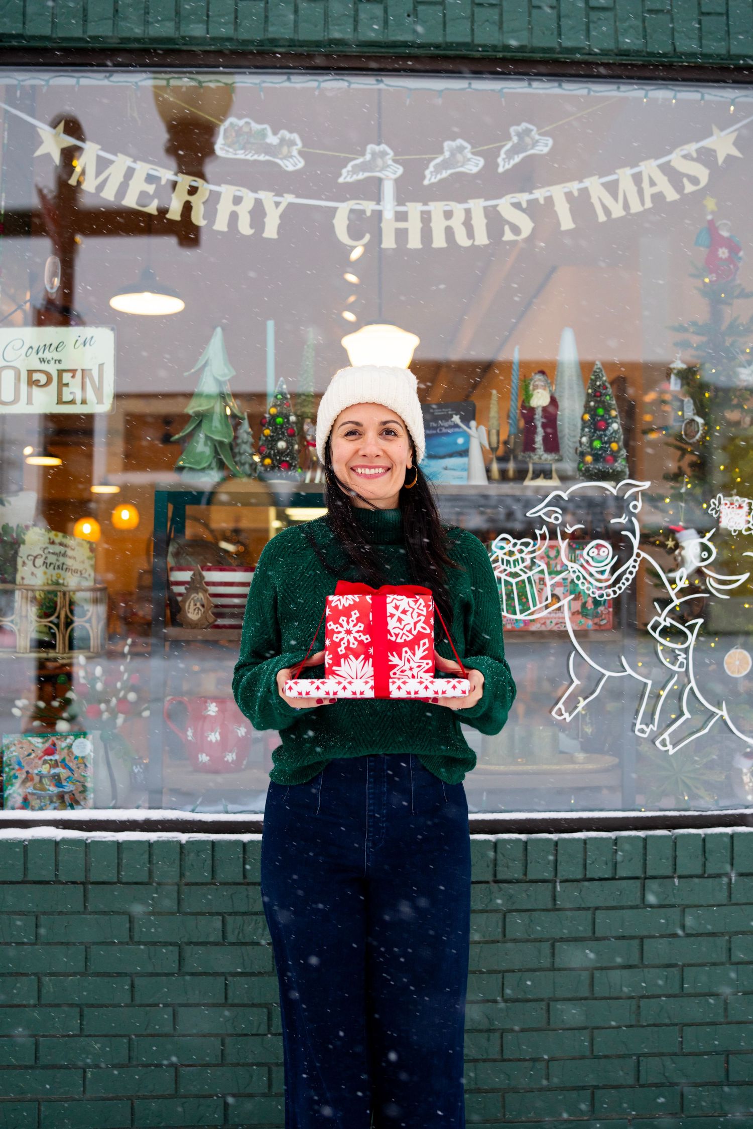 Festive storefront with Christmas decorations and window paintings in snowy weather.