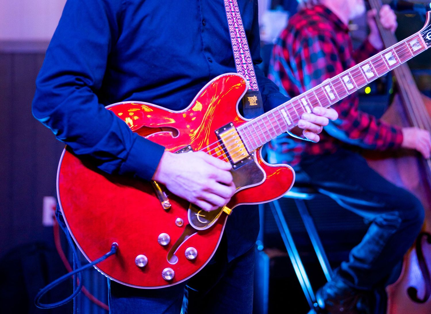 Musician playing a bright red Gibson electric guitar on stage in blue lighting.