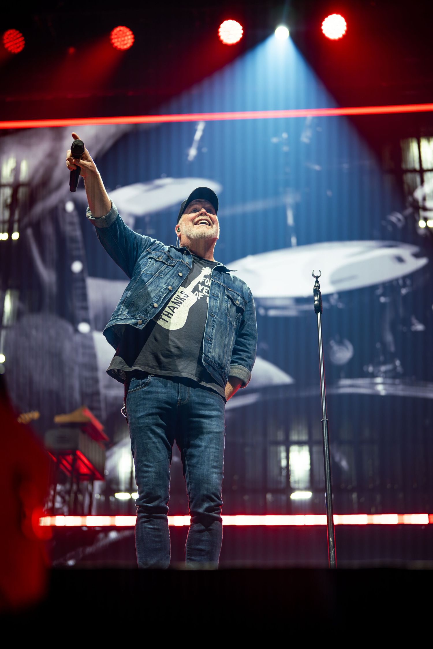 A performer in denim outfit sings passionately on stage with dramatic red and blue lighting effects.