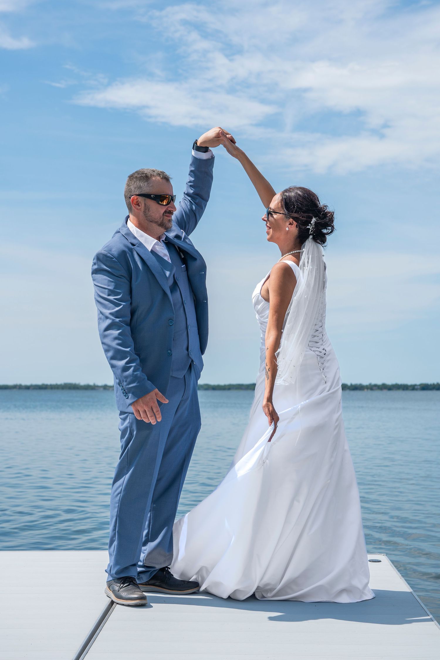Wedding couple shares candid moment on boat dock with beautiful water and sky backdrop.