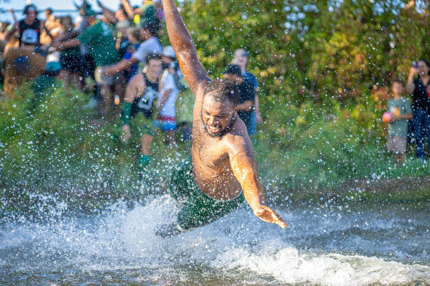 People jumping and splashing in water with trees in background after football game.