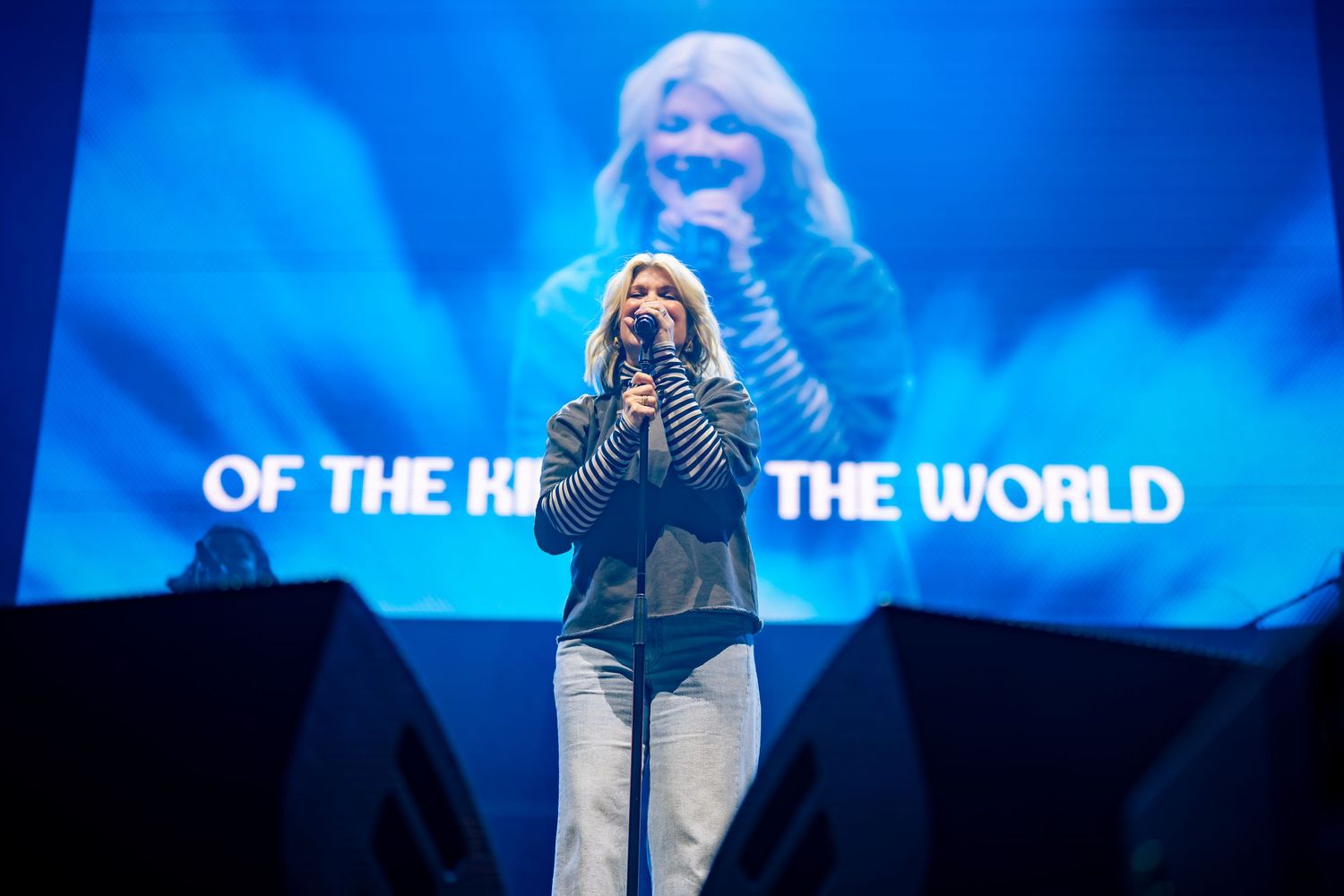 Stage performance with blue lighting and text projections on large display screen.