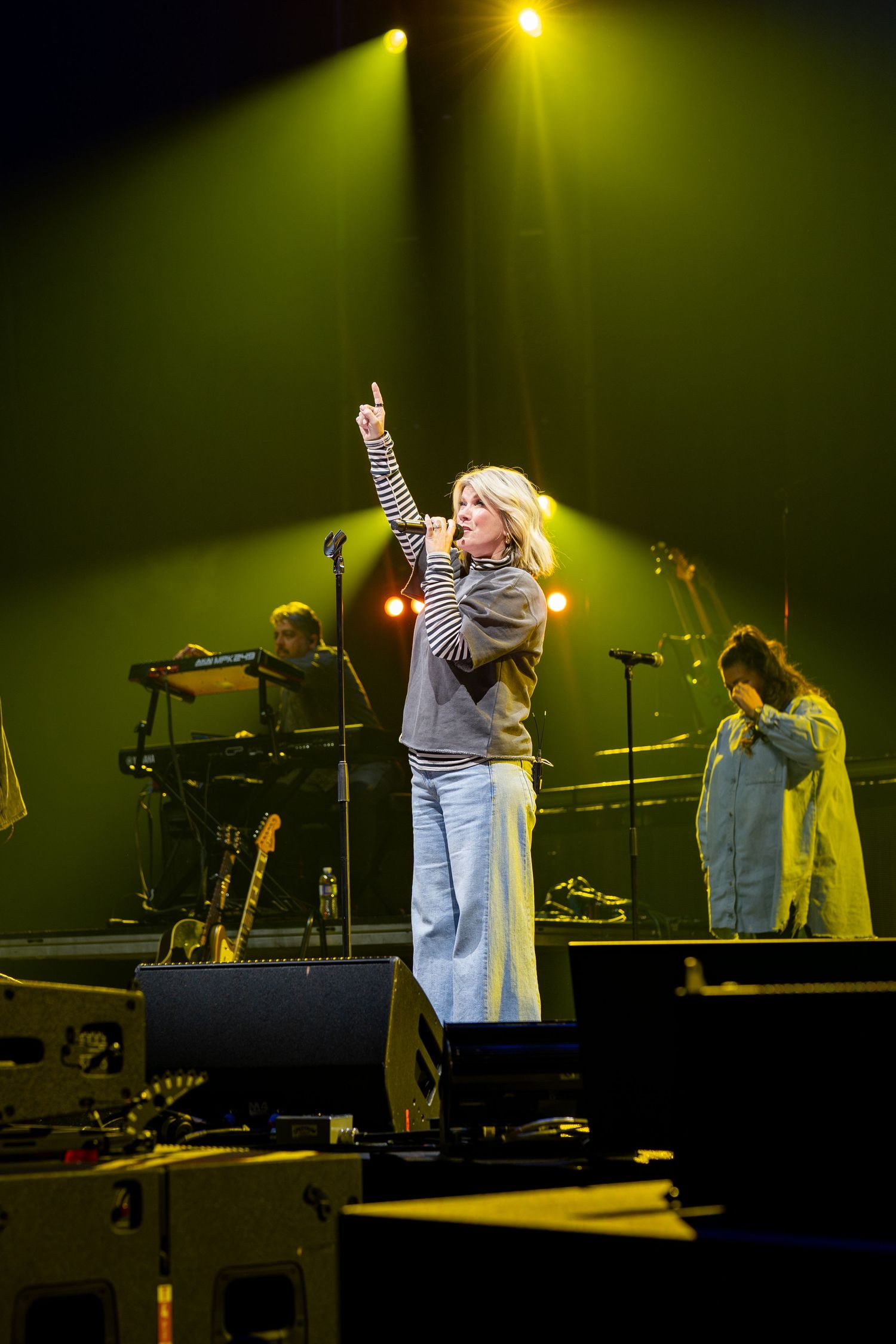 Concert performer in denim singing on stage under dramatic yellow lighting.