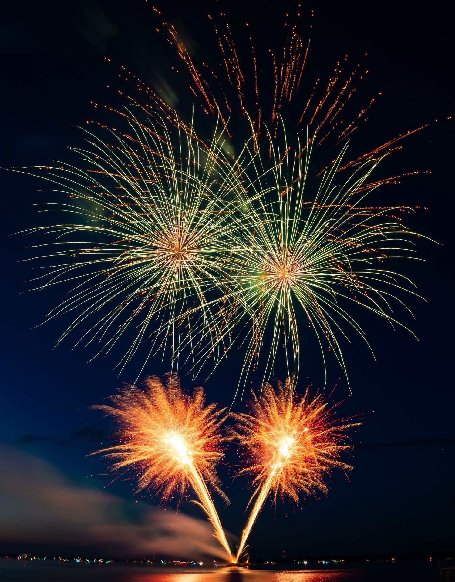 Bright green and gold fireworks bursting in the night sky over a waterfront during 4th of July.