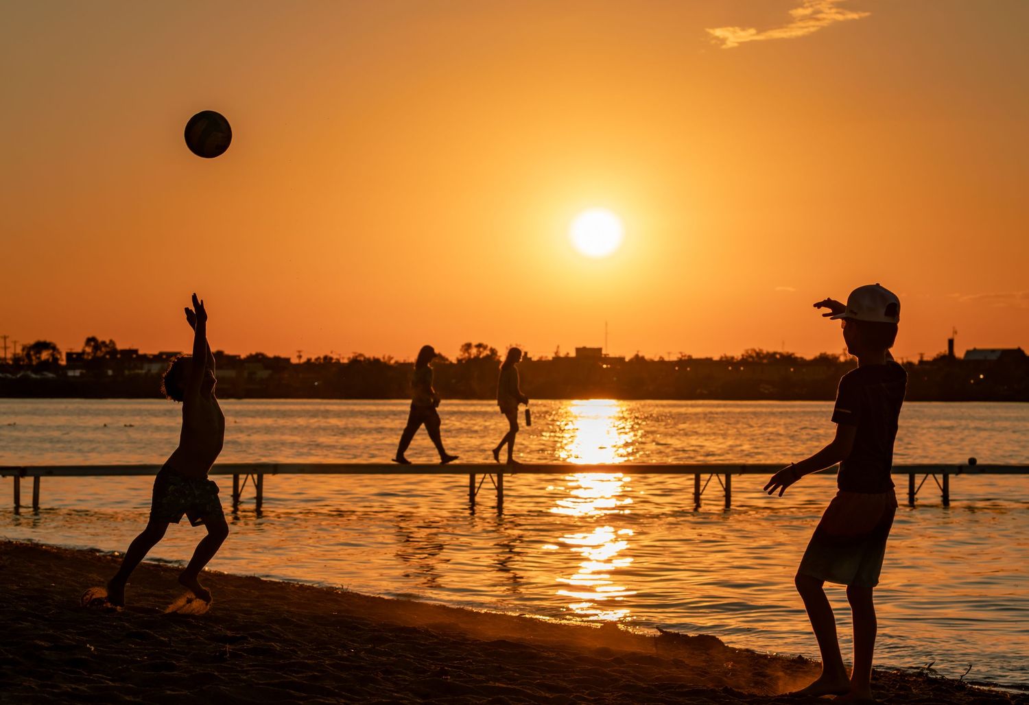 People playing and enjoying activities on a beach at sunset with golden orange sky.