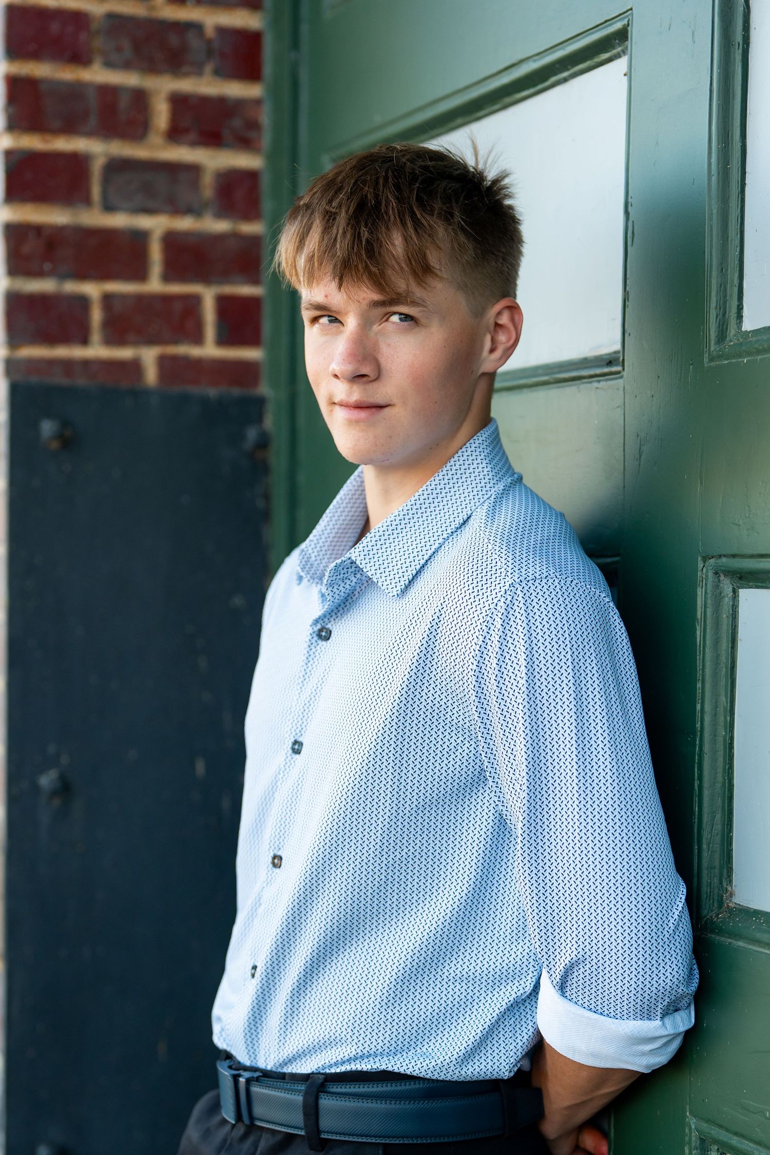 Young person in light blue dress shirt leaning against green door.