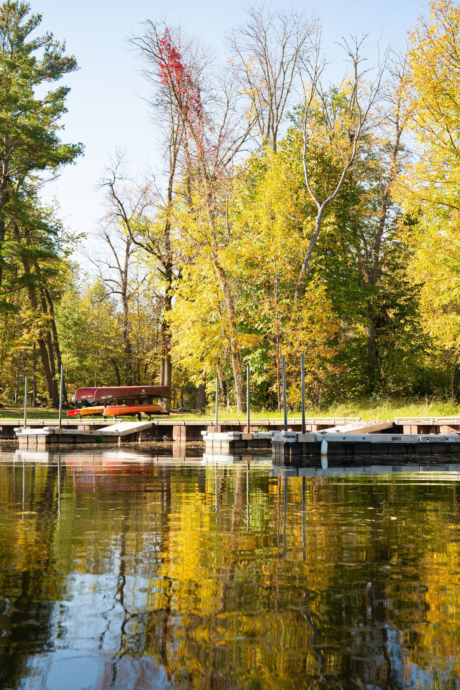 Autumn trees reflect in calm lake water with dock structures visible.