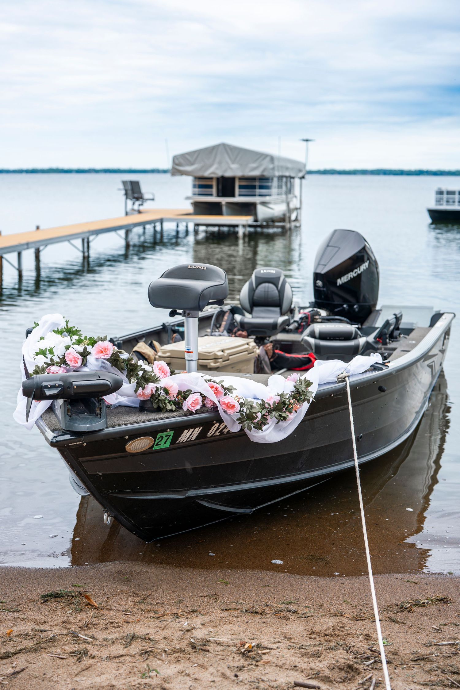 Row of fishing boats decorated with flowers docked at a lakeside pier during wedding.