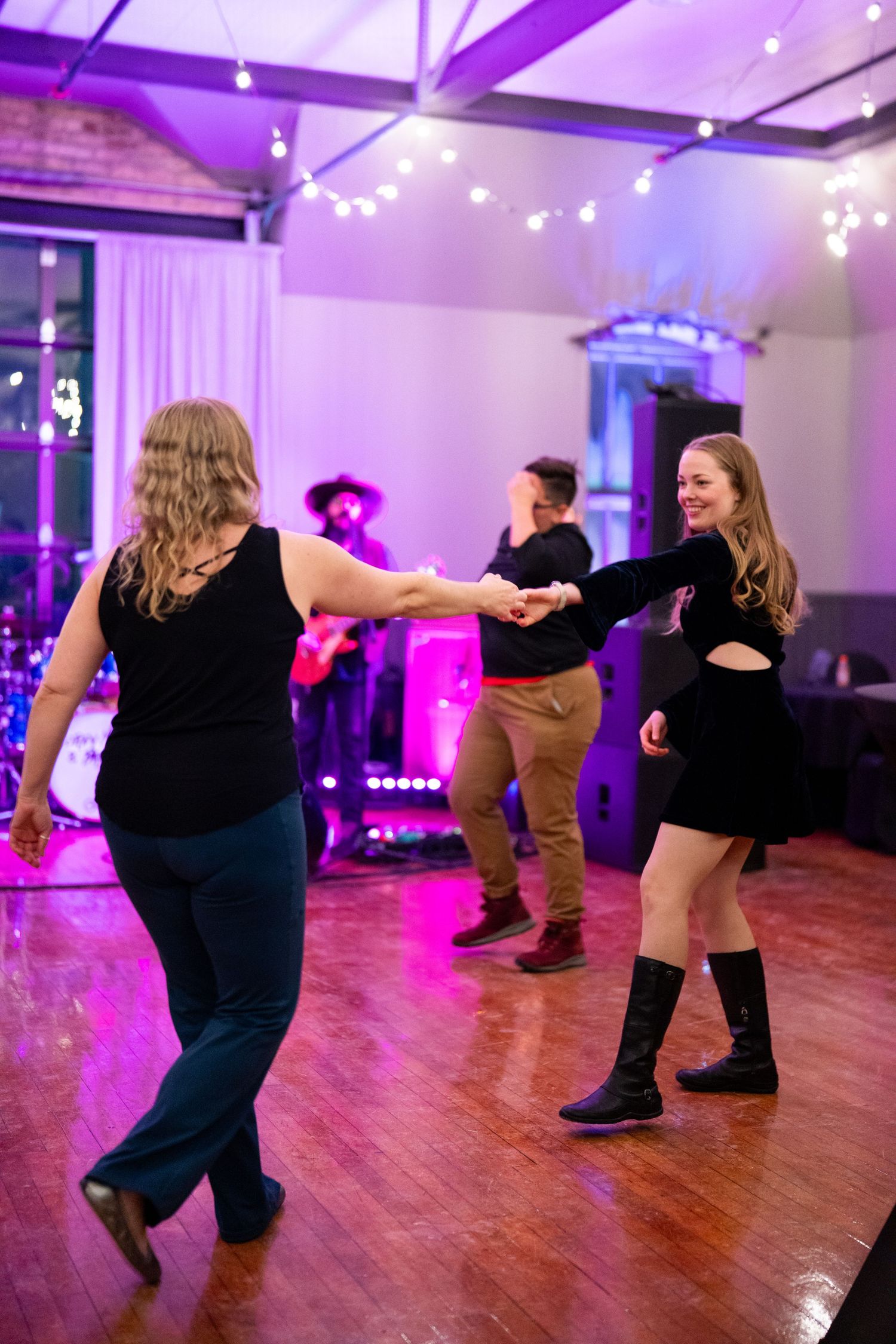 People dancing on a wooden floor at an event with purple mood lighting.