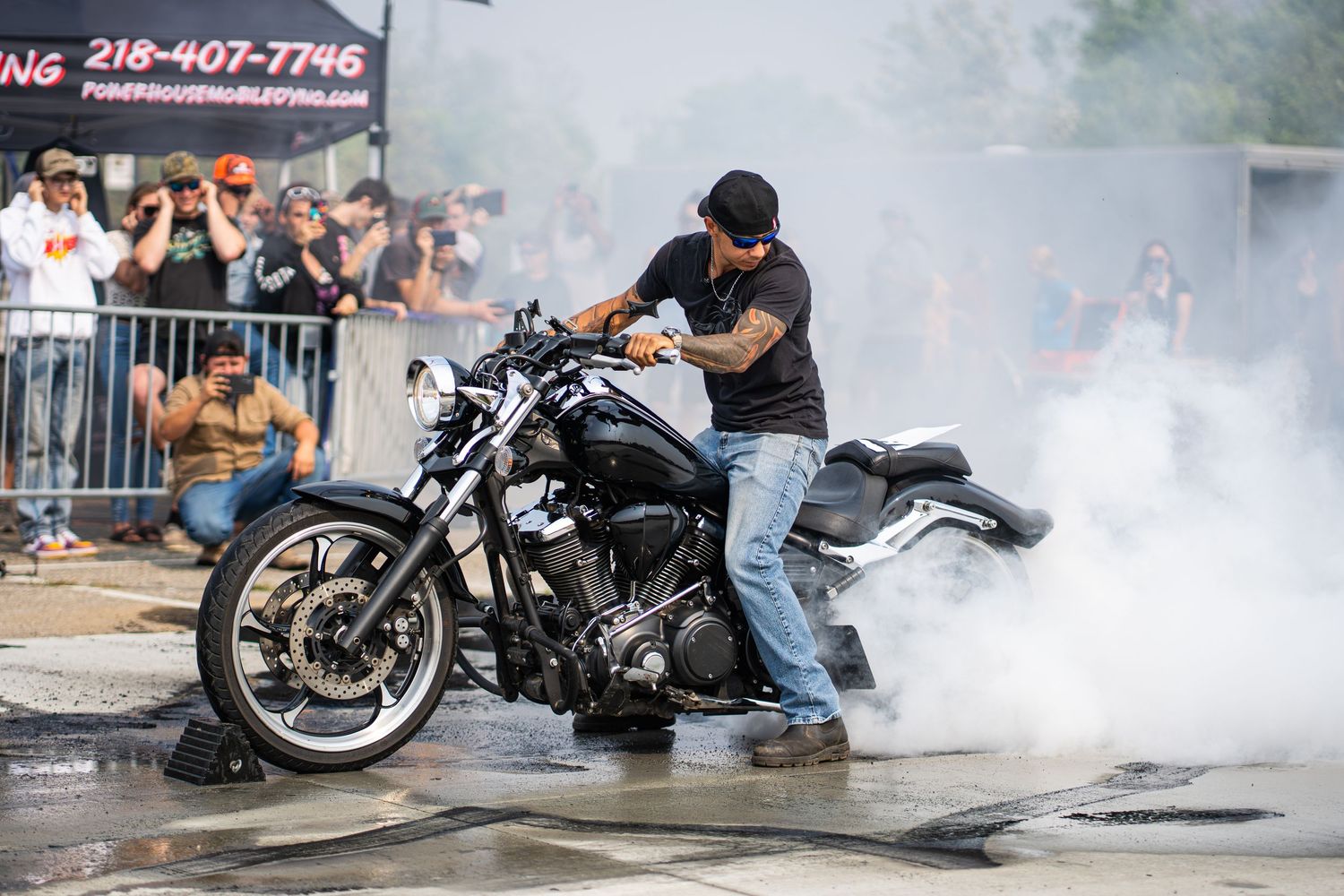 Motorcycles performing tire burnouts creating clouds of white smoke at a motorsports event.