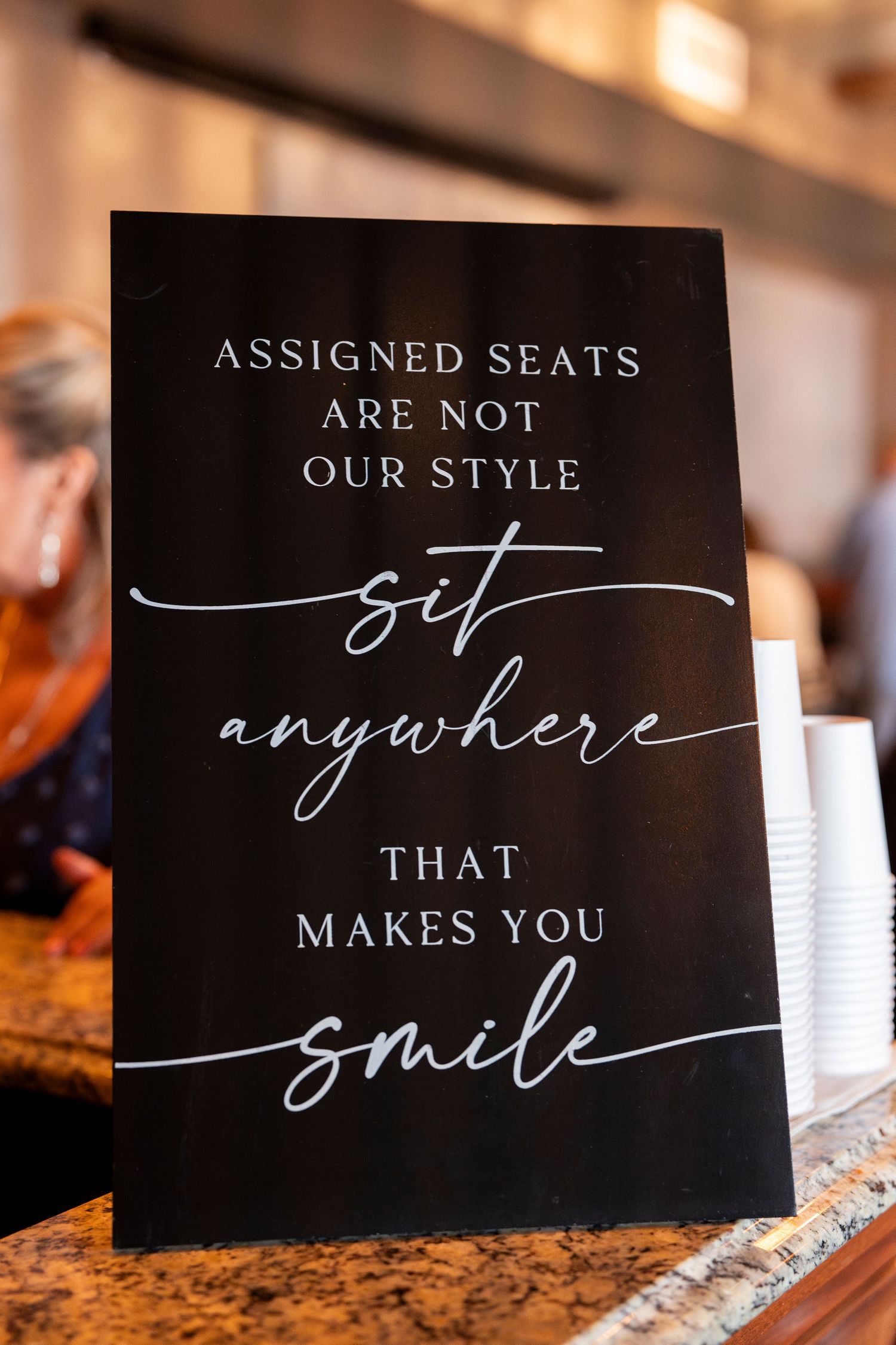 Black wedding signs with elegant white script encouraging guests to sit anywhere that makes them smile.