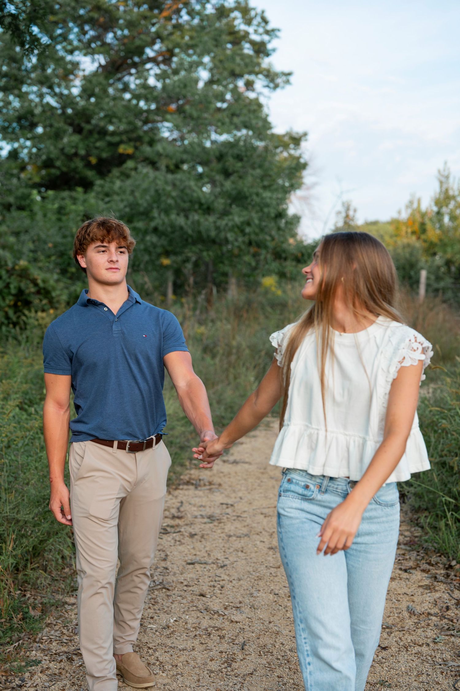 A couple walking hand in hand down a nature trail surrounded by trees.