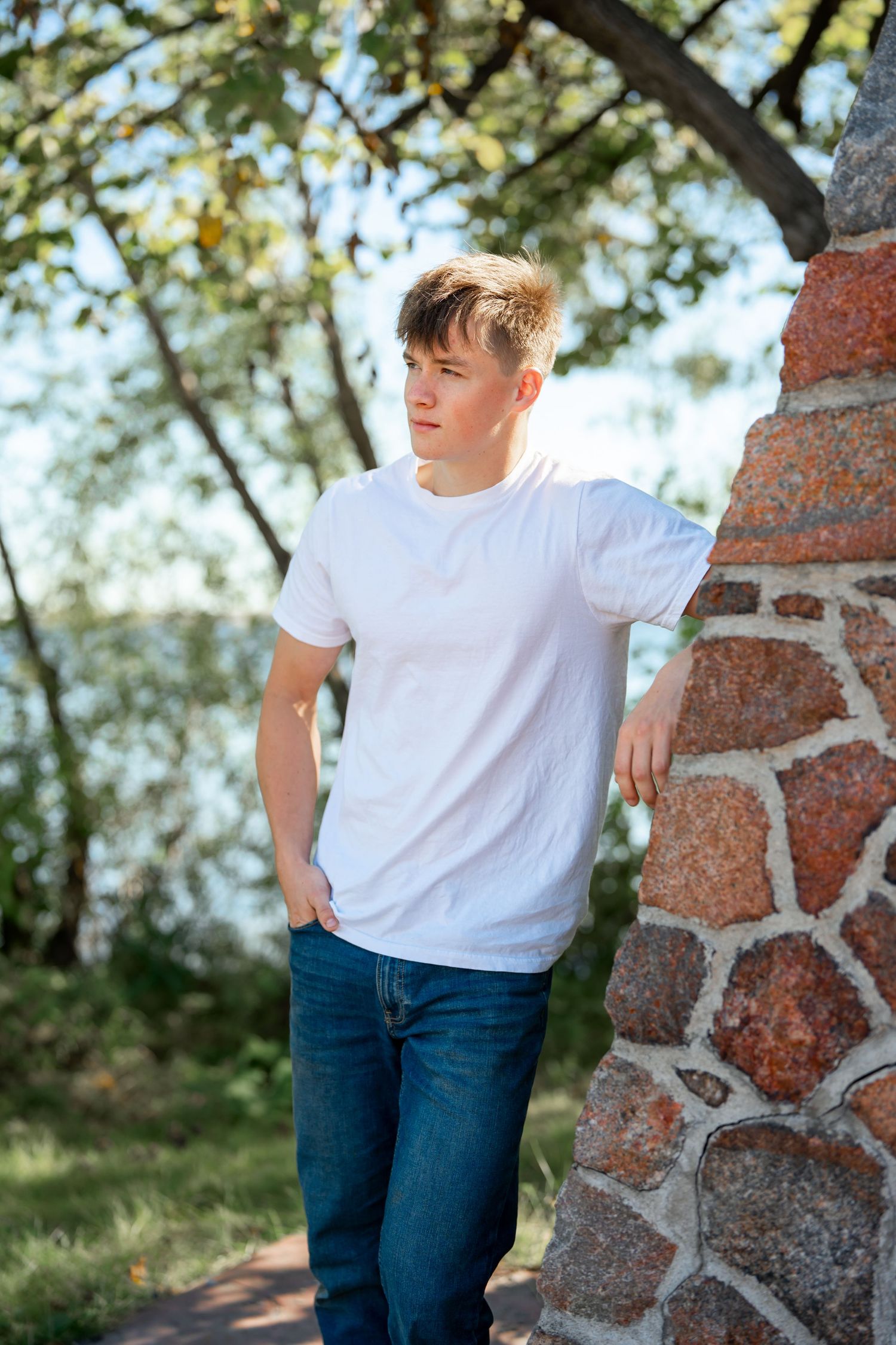 Casual outdoor portrait of man in white t-shirt leaning against stone wall.