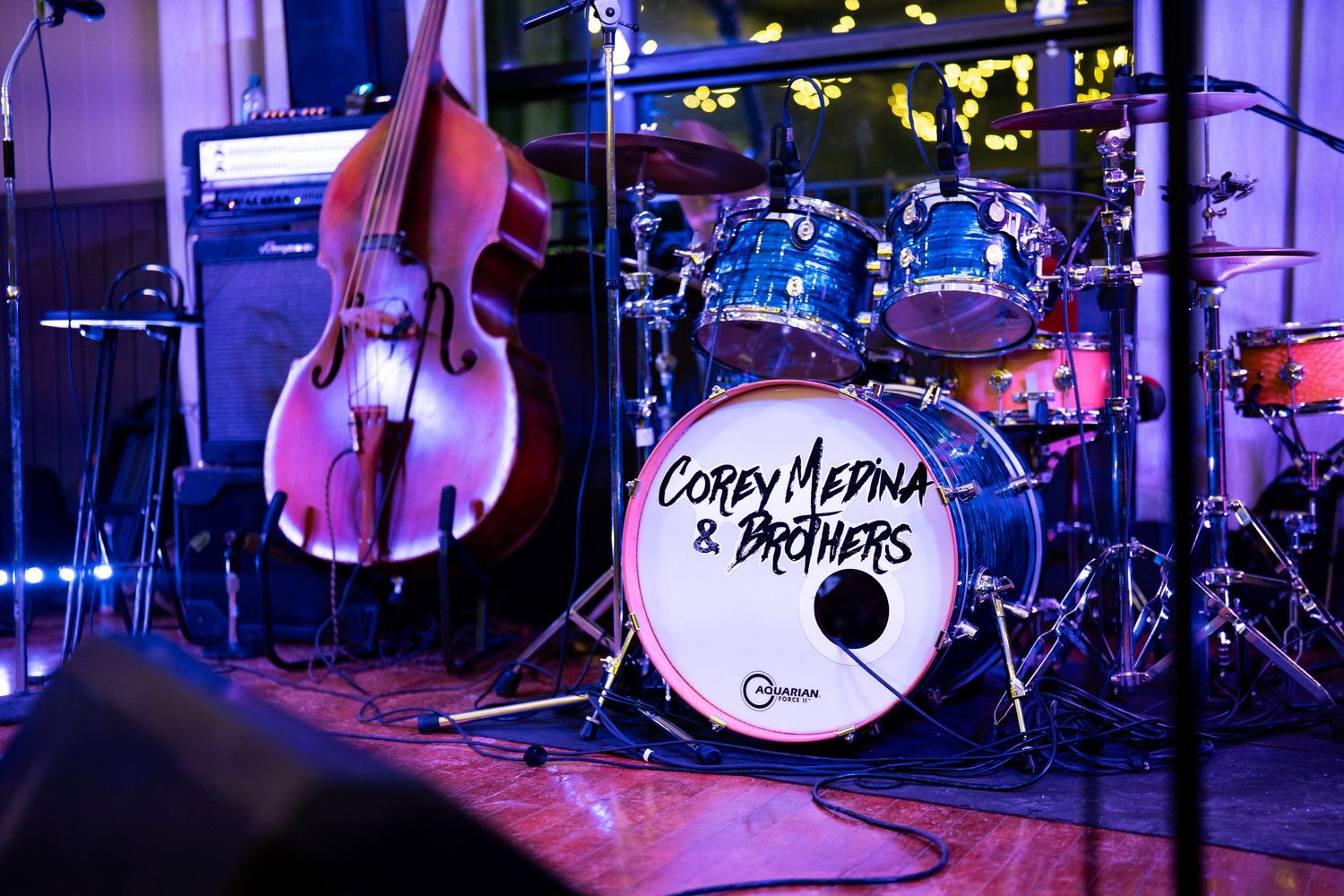 Musical stage setup with drum kit and instruments illuminated in purple lighting.