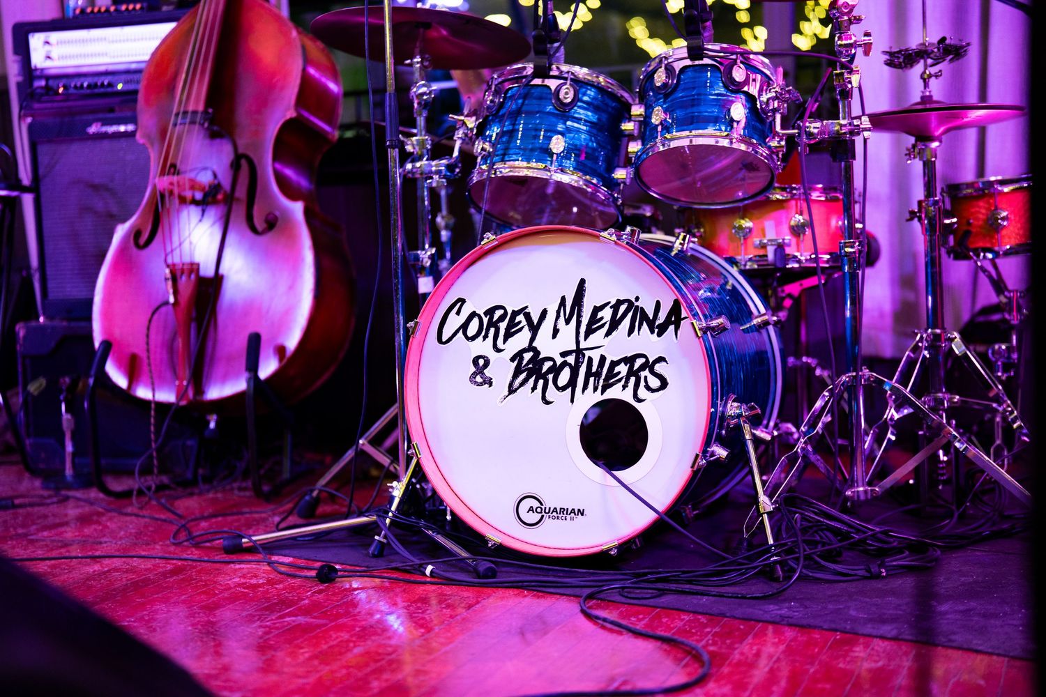 Drum kit and upright bass on stage with purple lighting and band name on bass drum.