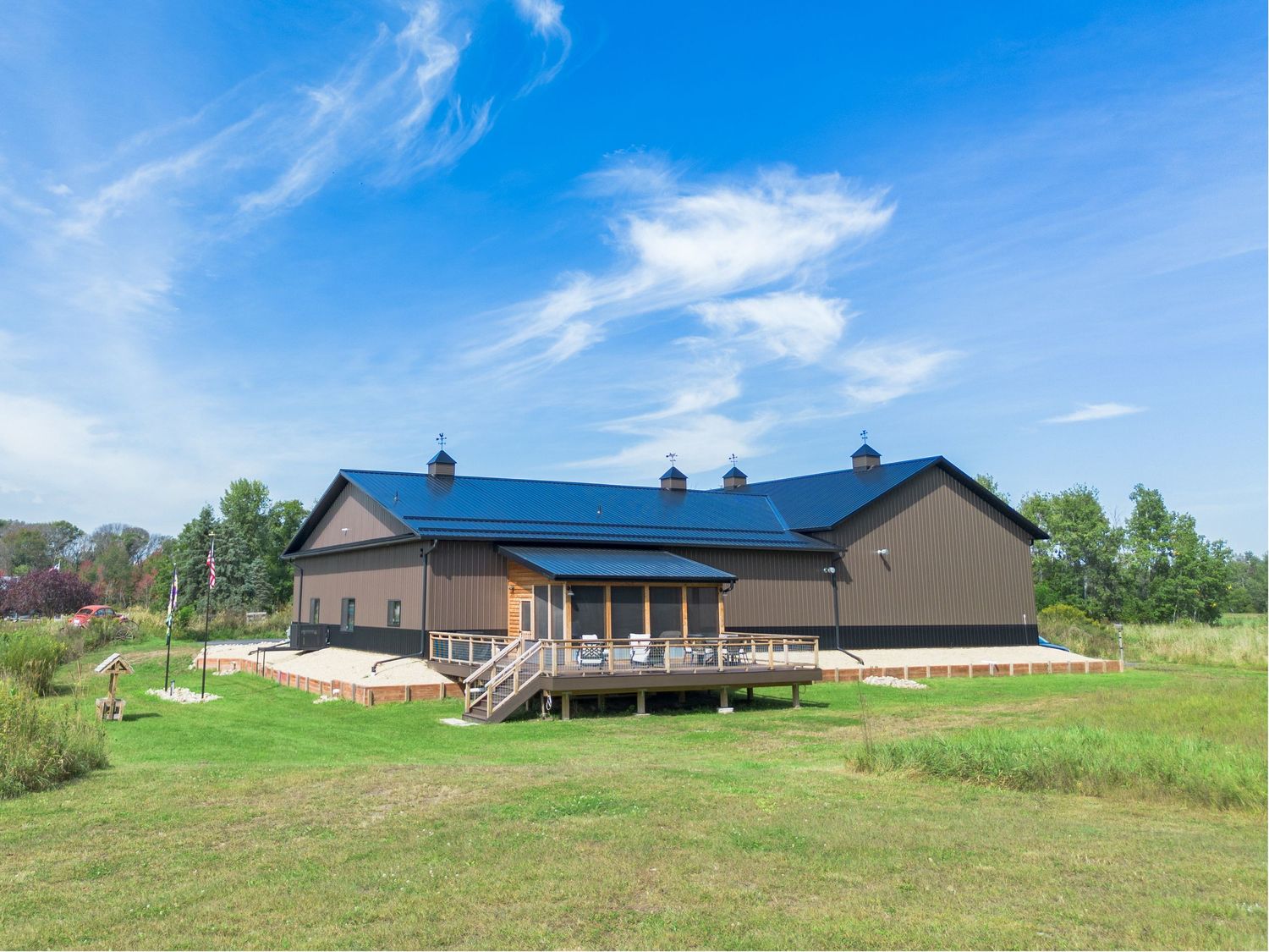 Panoramic view of a modern ranch-style building with blue roof against a bright summer sky.