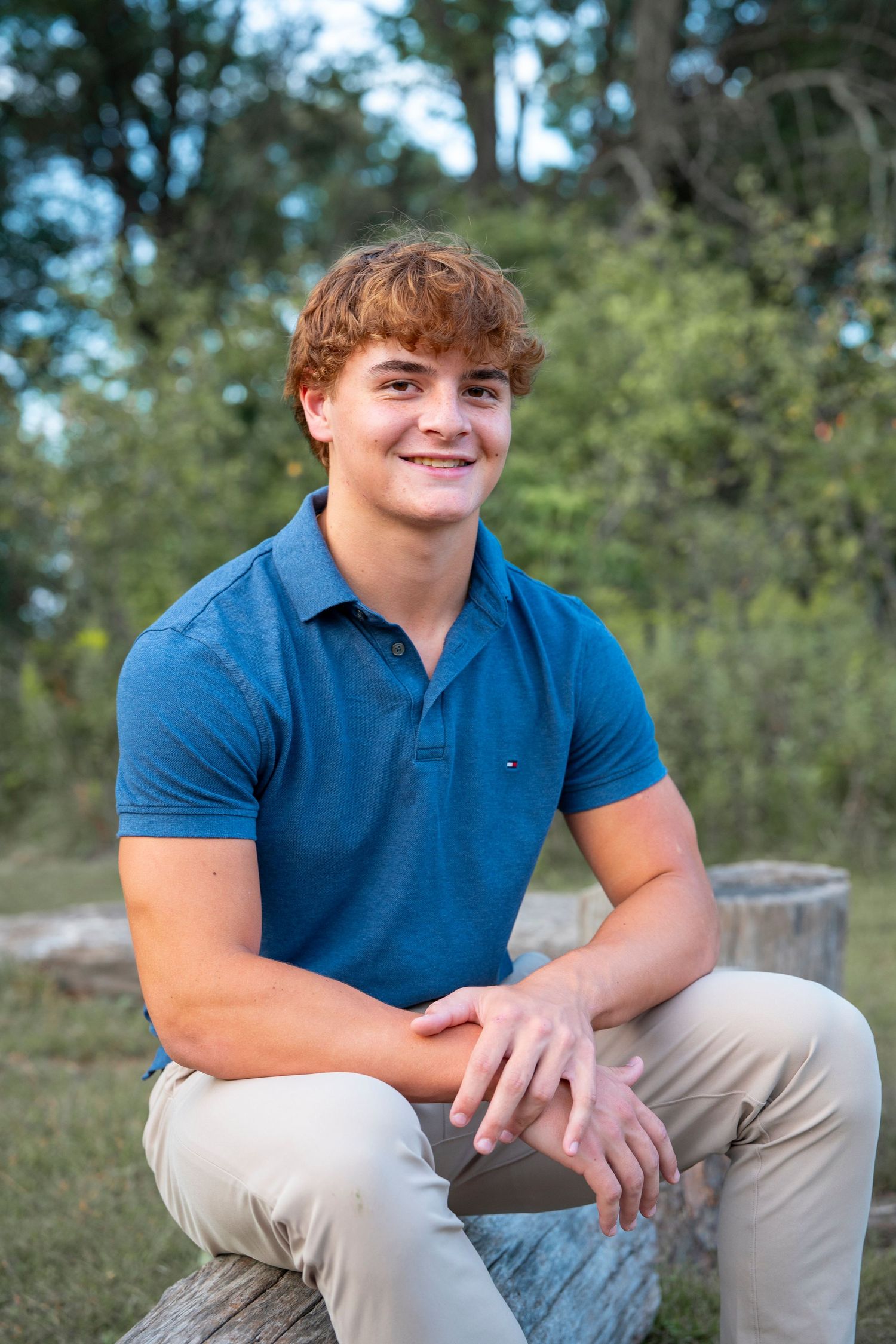 Casual outdoor senior portrait sitting on a log in blue polo and khaki pants.