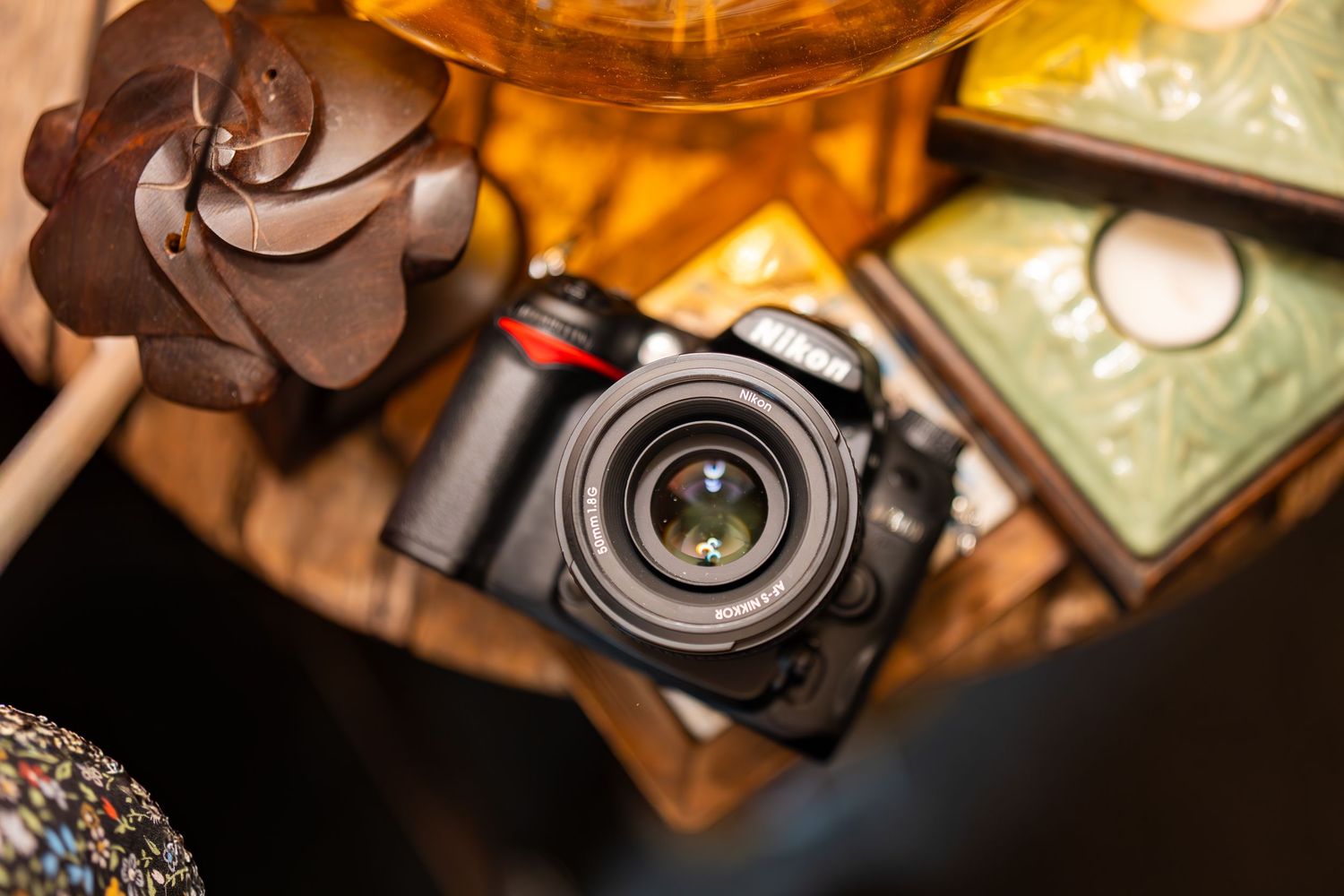 A Nikon DSLR camera resting on a wooden table surrounded by decorative items including a floral sculpture.