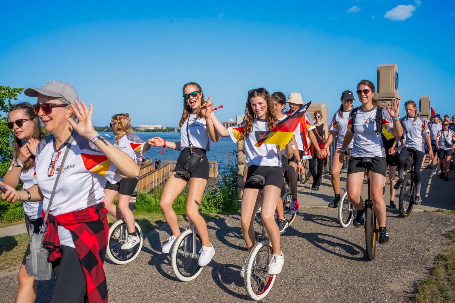 Large group of unicyclists riding together on waterfront path during summer event.