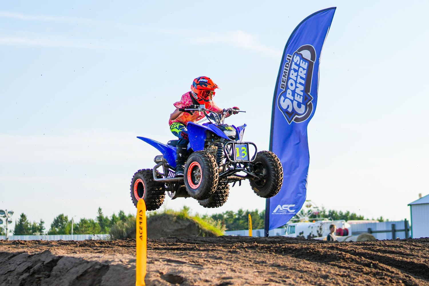 ATV riders performing impressive jumps over dirt mounds at an outdoor motorsports event.