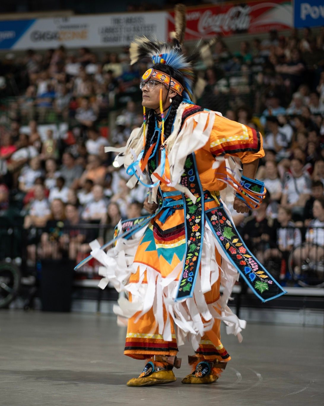 Native American dancers in traditional regalia performing at a powwow celebration.