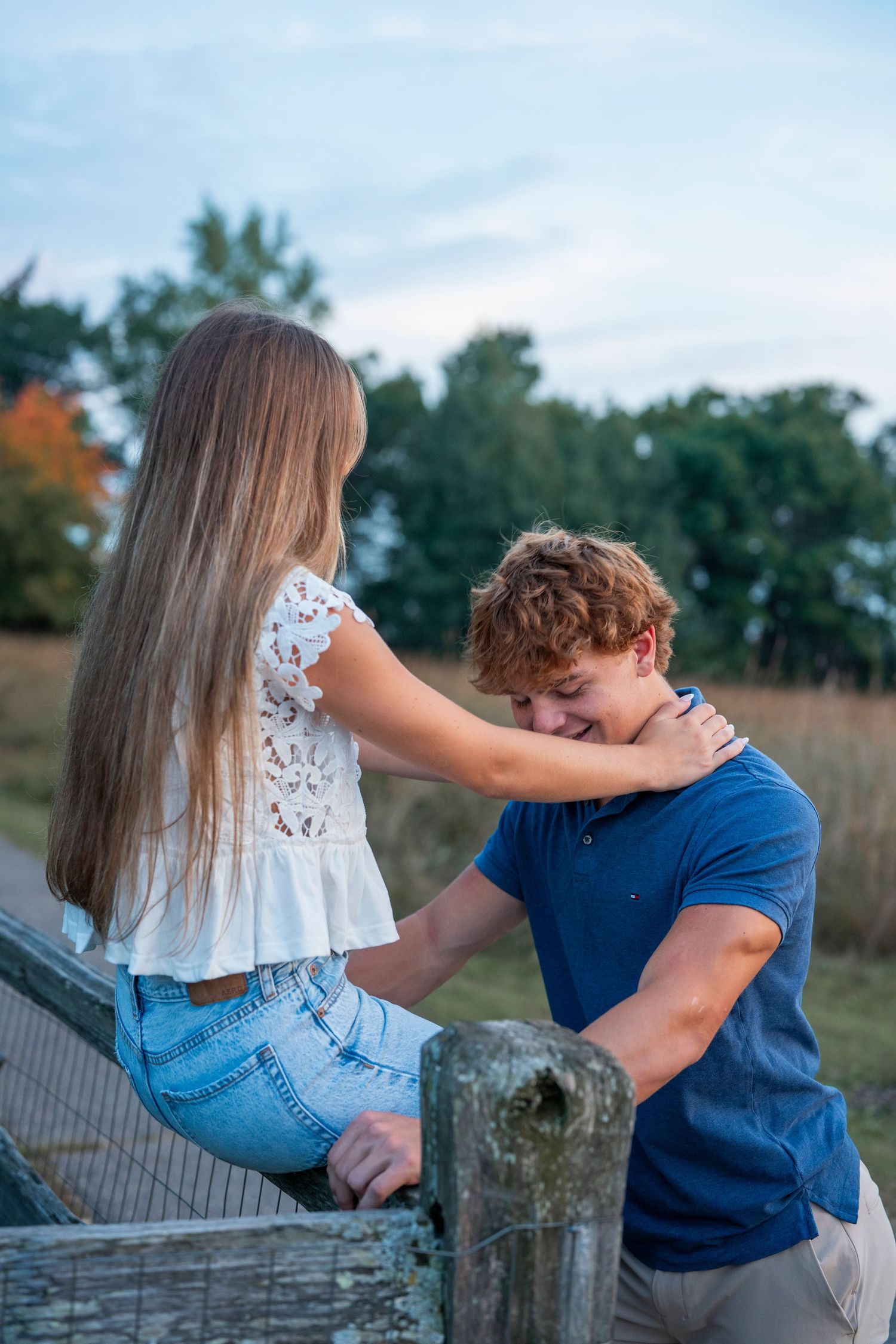 A romantic couple shares an intimate moment by a rustic wooden fence in a rural outdoor setting.