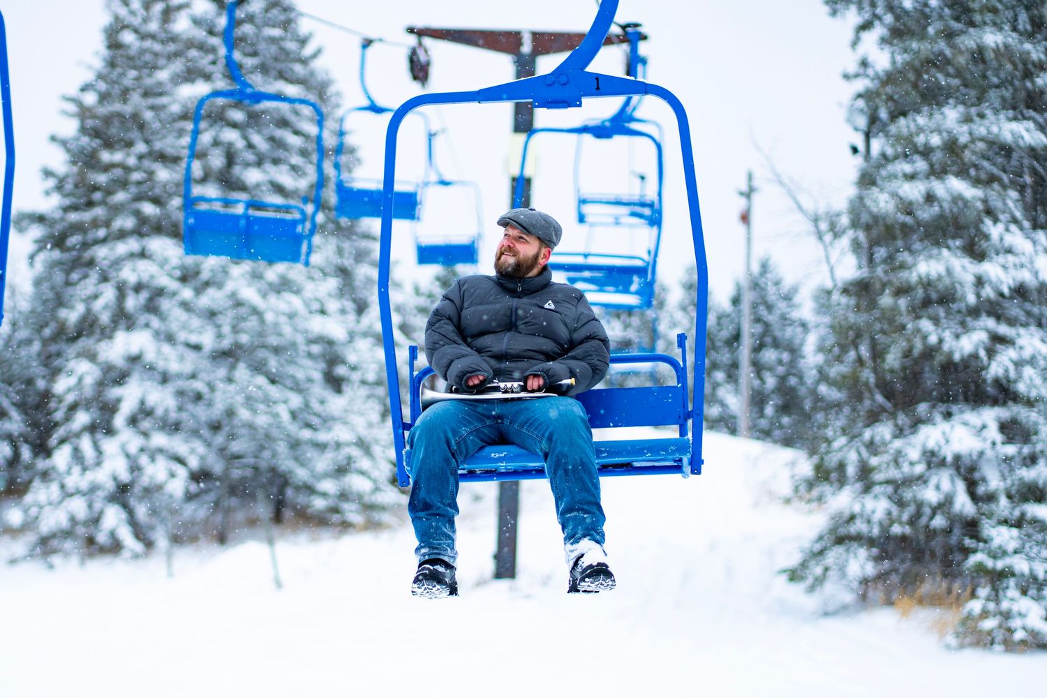 Empty ski lift chairs moving across a snowy winter landscape with evergreen trees.
