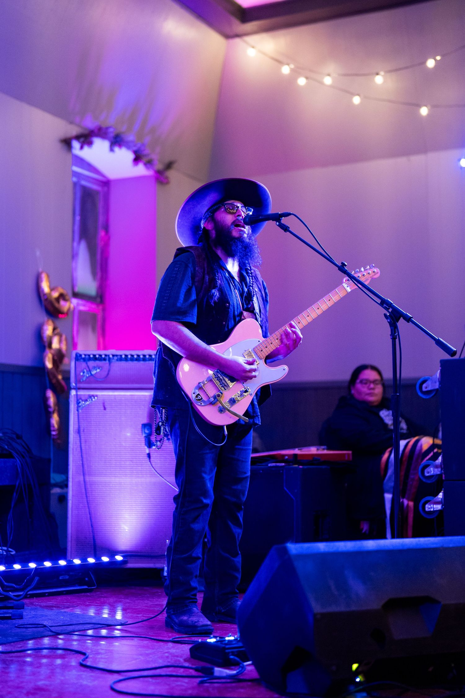 Guitarist performing on stage with purple lighting and string lights in the background.