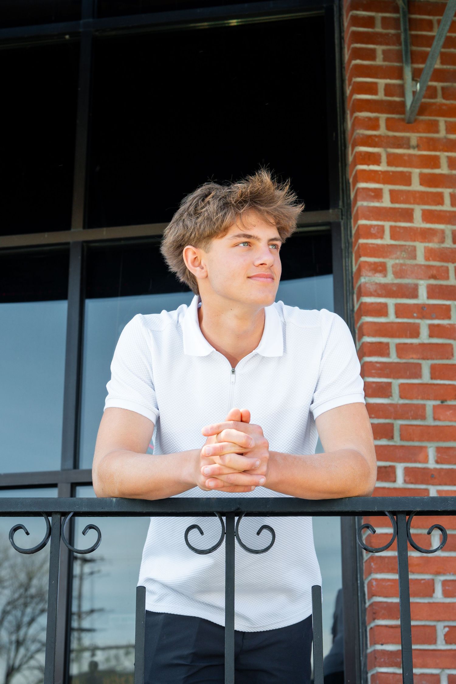 Person in white shirt leaning on brick balcony railing while looking off into distance.