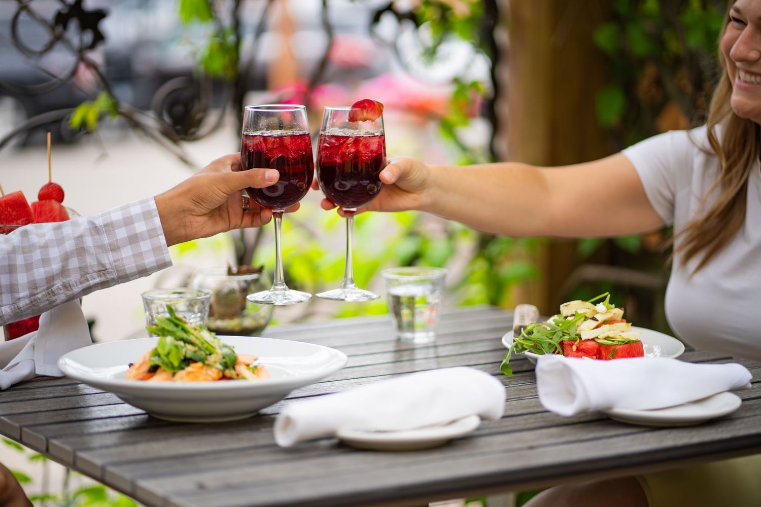 Close-up of hands cheersing drinks at outdoor dining table.